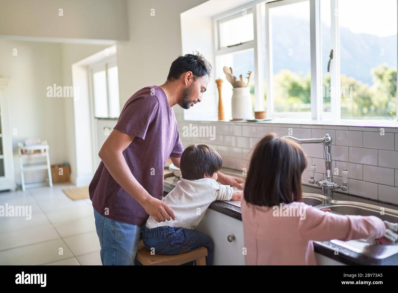 Padre e bambini che fanno piatti al lavello della cucina Foto Stock