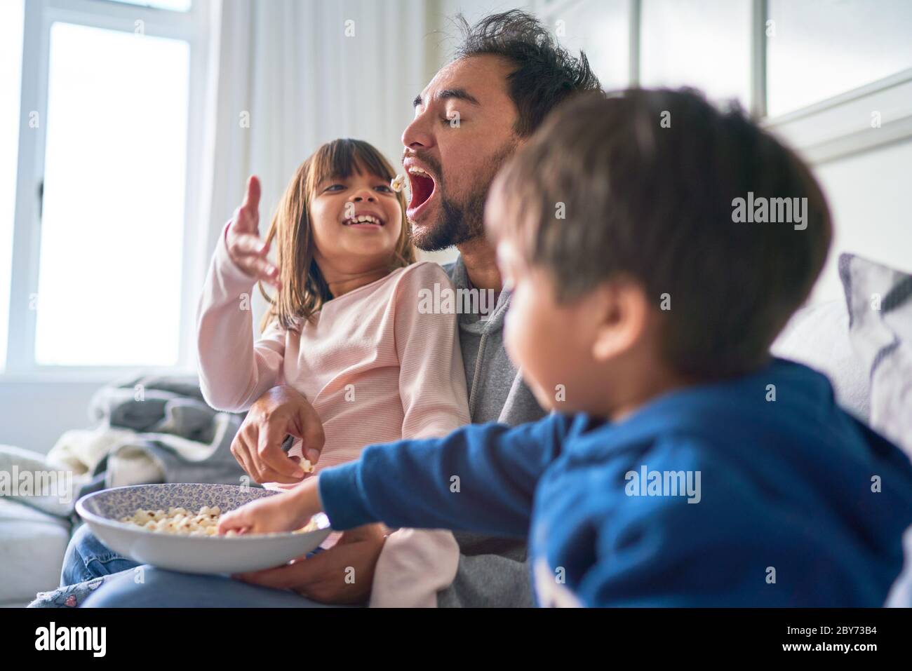 Bambini giocosi che temono il papcorn del padre sul divano Foto Stock