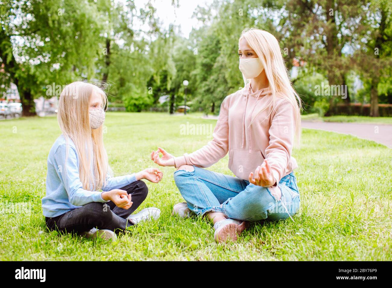 Madre e piccolo cattiviere del parco indossando maschere protettive. Mamma che insegna yoga ragazza. Famiglia, giorno delle madri, pandemia di covidio Foto Stock