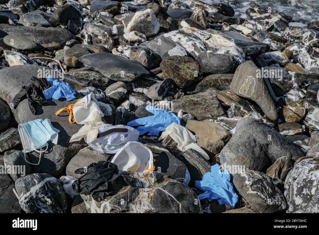 Rifiuti medici, maschera virus e guanti di plastica spazzatura scartata sulla costa rocciosa del mare, coronavirus covid19 inquinamento Foto Stock