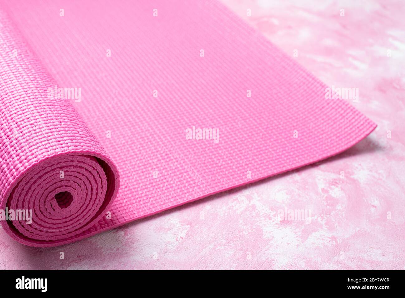Tappetino yoga su sfondo rosa. Attrezzature per yoga. Concetto stile di vita sano, sport, meditazioni e relax. Vista dall'alto, spazio di copia Foto Stock