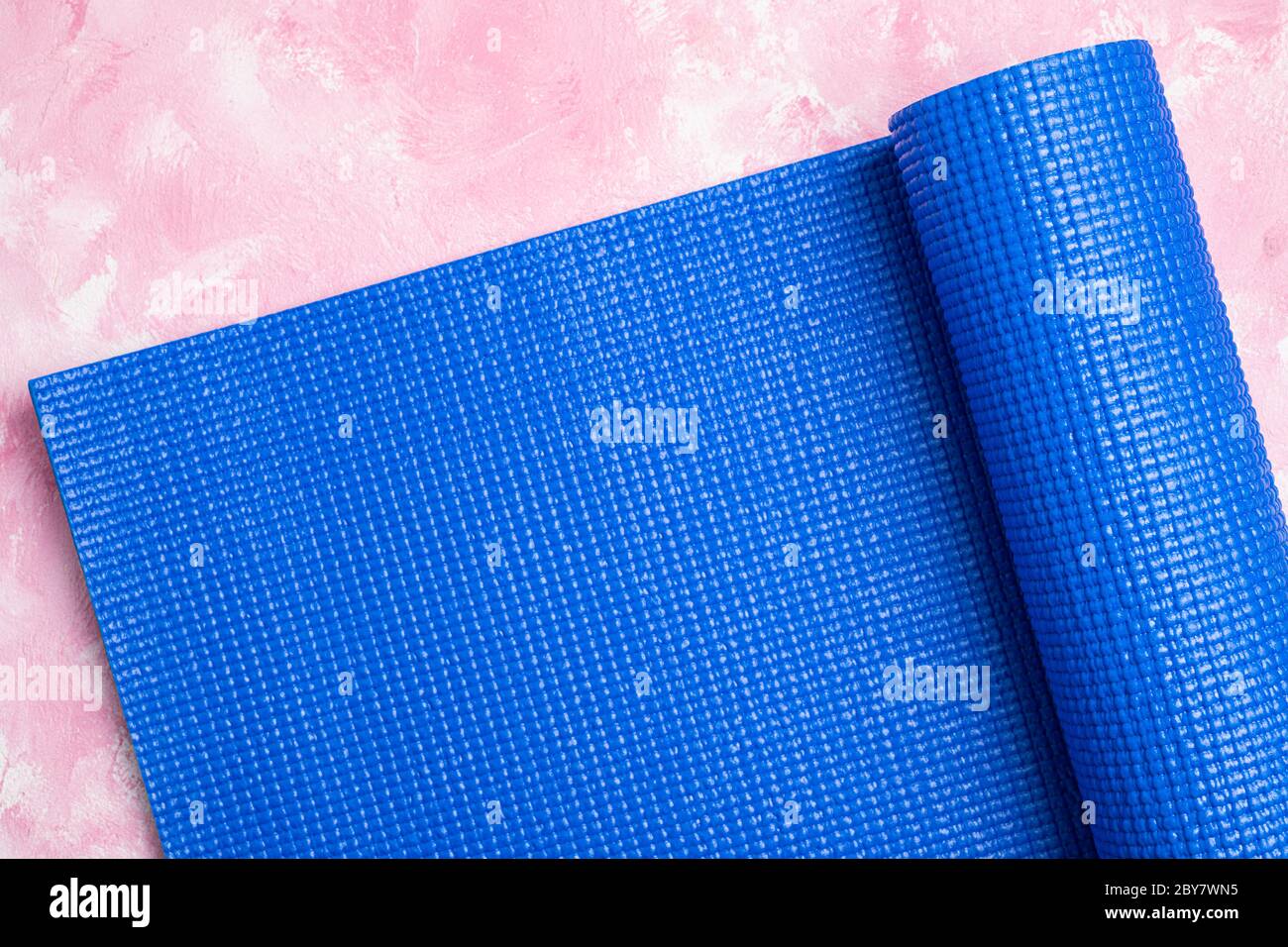 Tappetino blu per yoga su sfondo rosa. Attrezzature per yoga. Concetto stile di vita sano, sport, meditazioni e relax. Vista dall'alto, spazio di copia Foto Stock