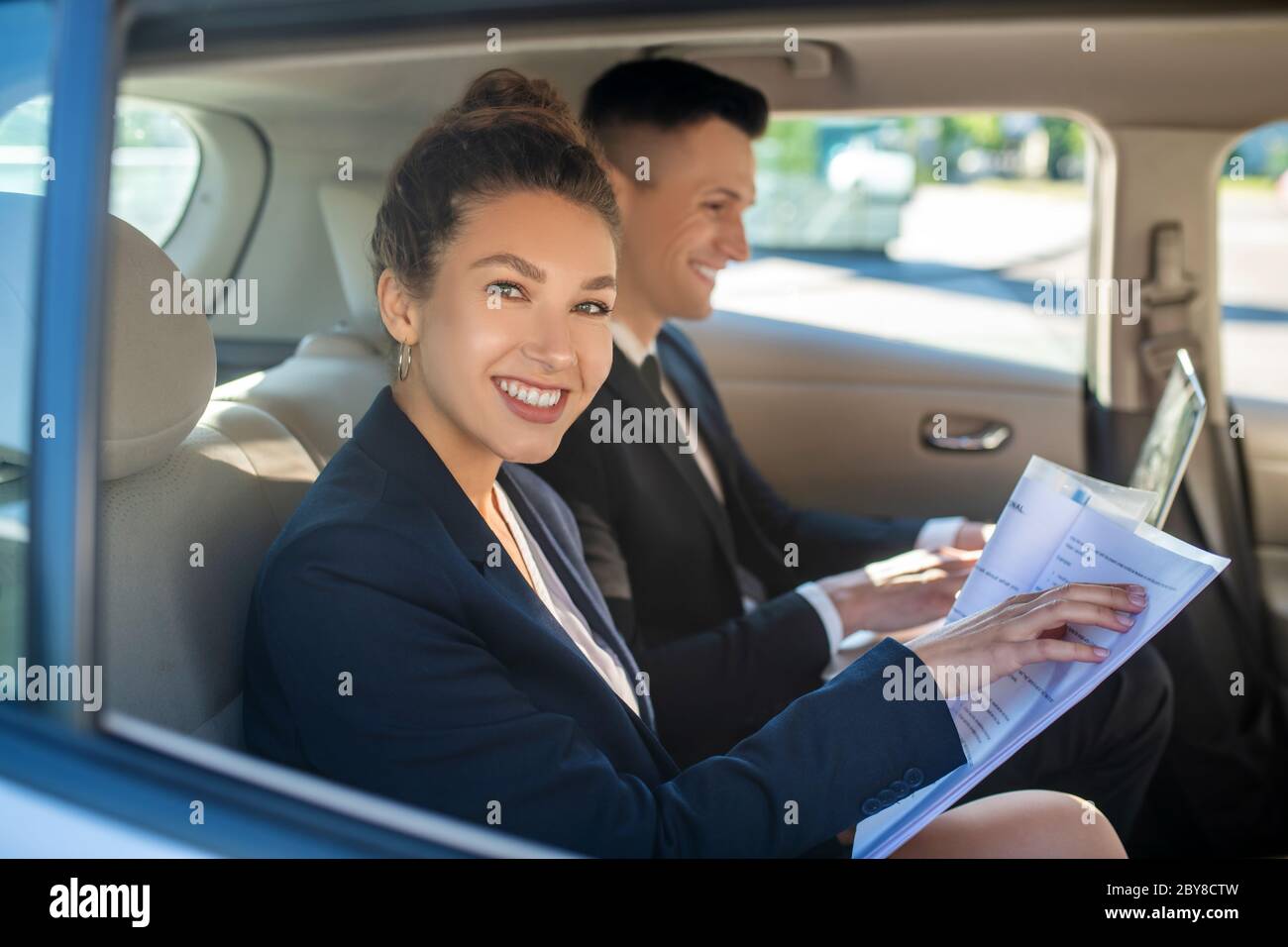Donna sorridente con carte uomo con computer portatile in auto Foto Stock