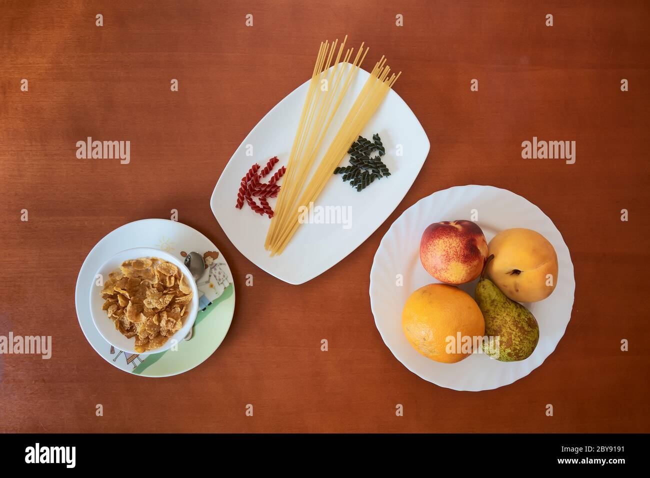 cereali, pasta e frutta su piatti bianchi e tavolo in legno Foto Stock