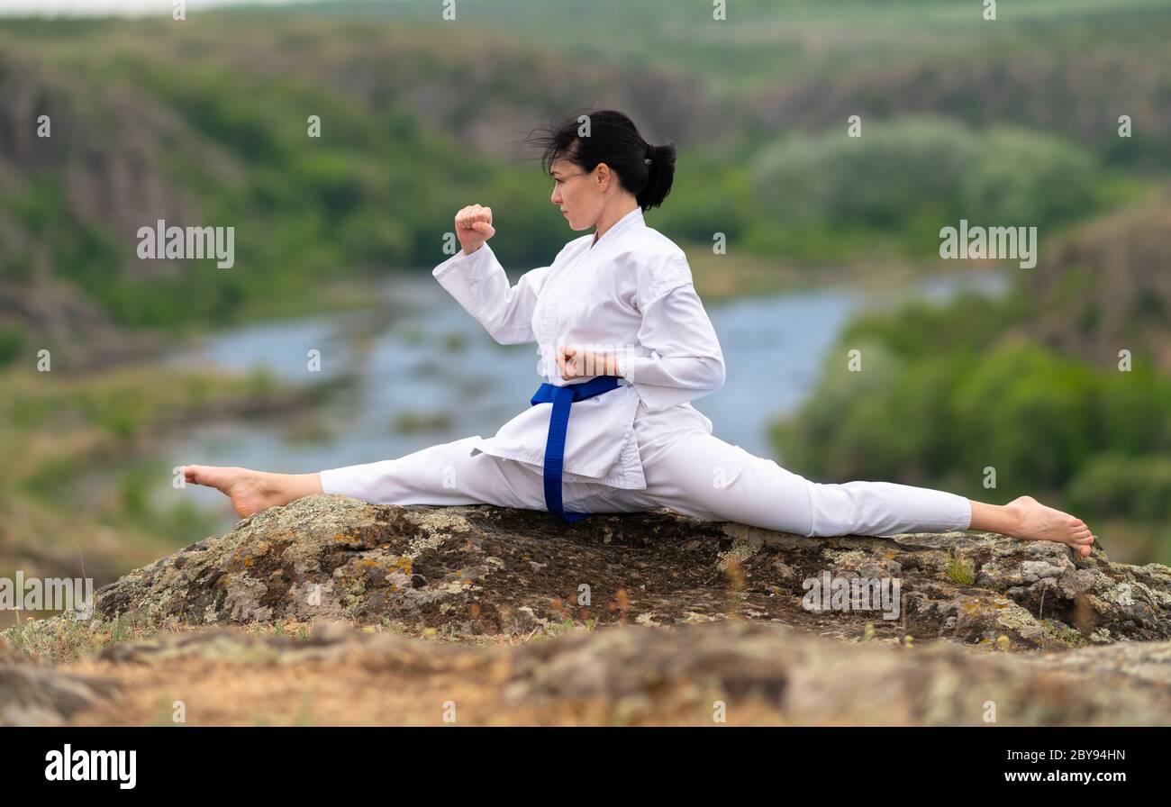 Giovane donna che si allea per il kickboxing facendo le divisioni per aumentare la sua mobilità e flessibilità su una roccia che domina una valle e un fiume Foto Stock