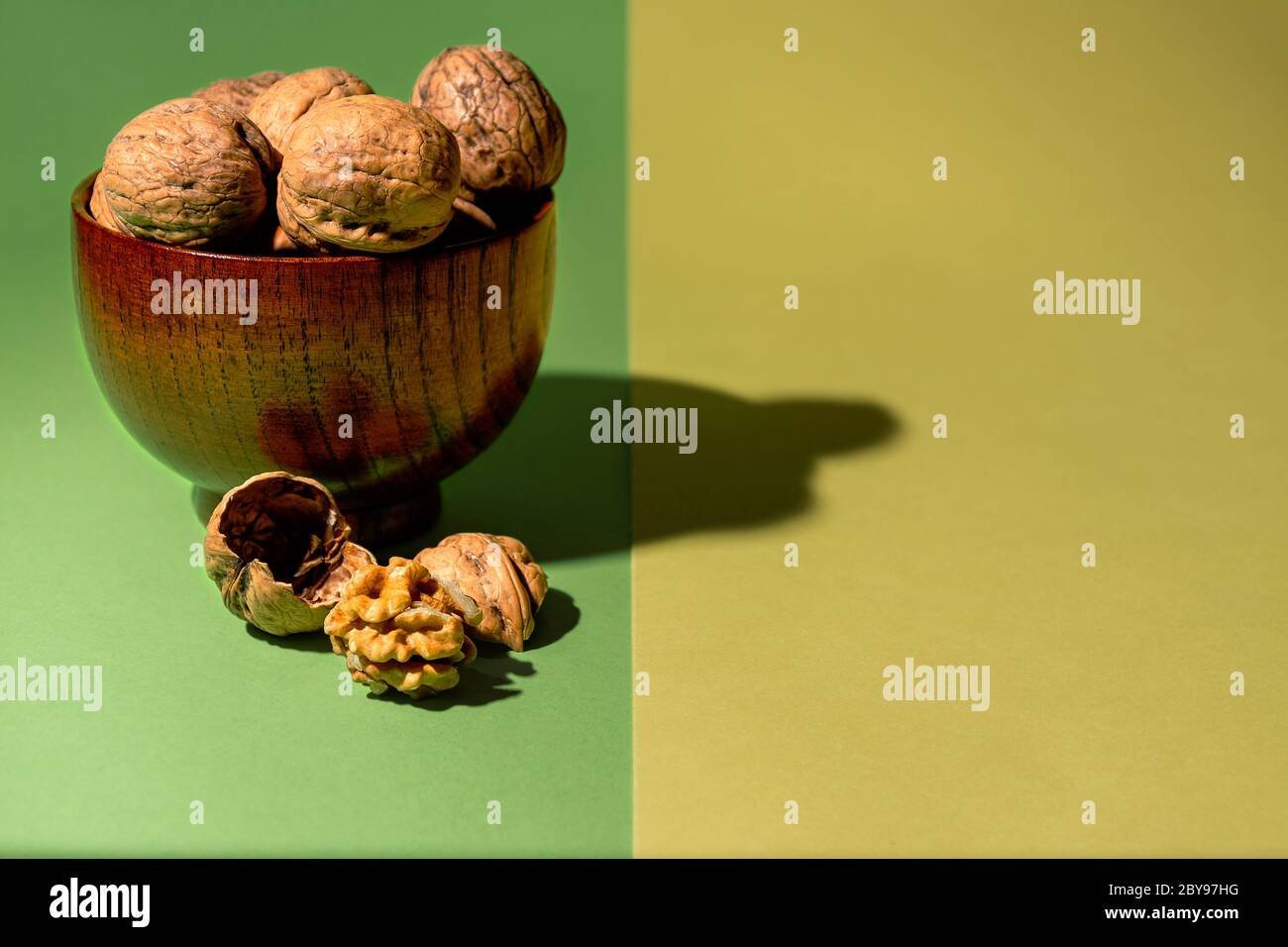 Ciotola di noci grezze accanto ad un dado senza guscio su sfondo verde e giallo Foto Stock