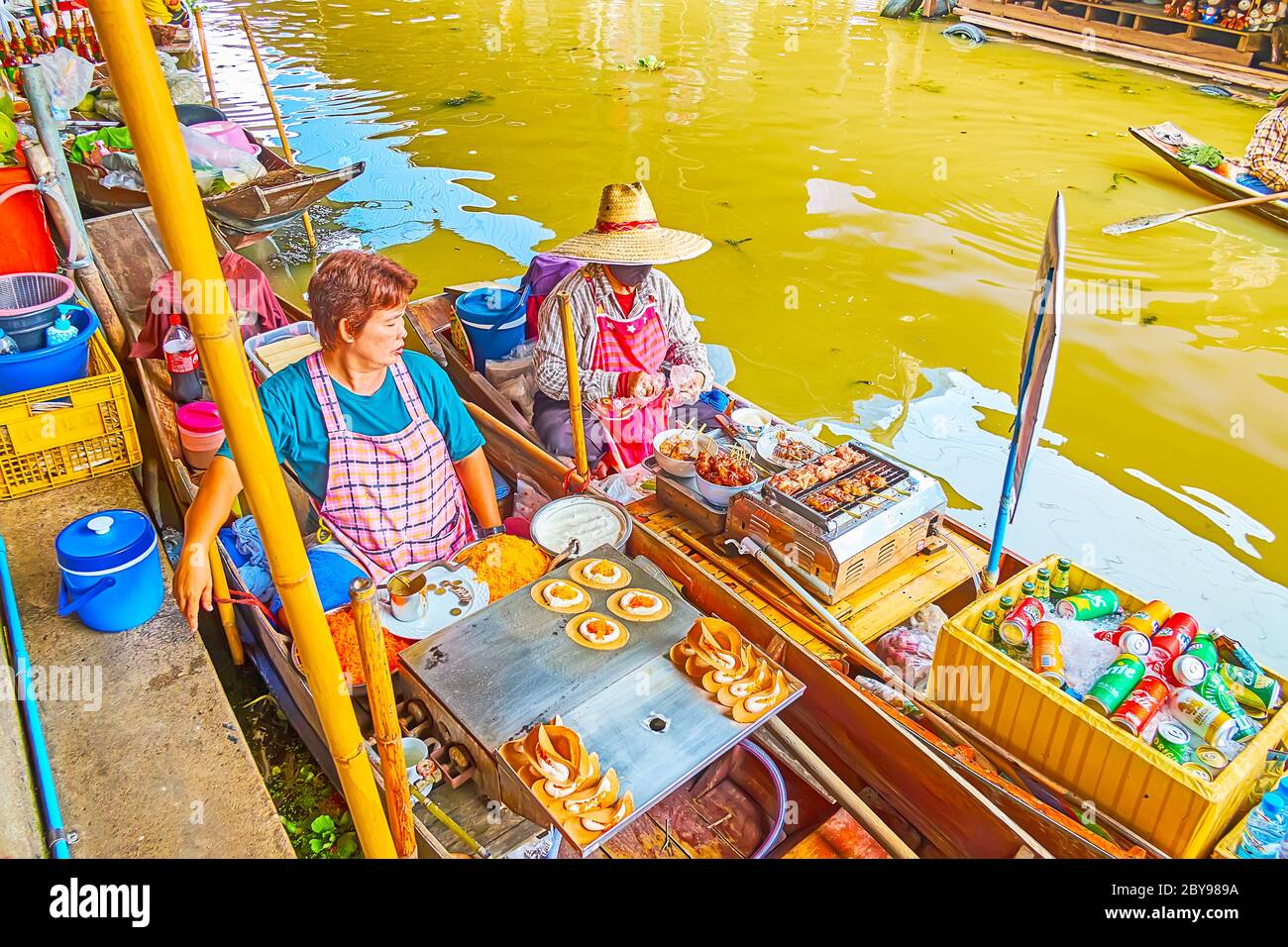 DAMNOEN SADUAK, THAILANDIA - 13 MAGGIO 2019: I venditori di cibo fanno frittelle croccanti (khanom buang) e maiale alla griglia su spiedini, seduti in barche sampan su Foto Stock