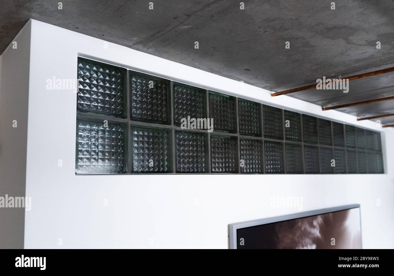 Un fresco-guardare basso costo mattoni di vetro o blocchi di vetro come un'aggiunta decorativa nella parete bianca sotto il soffitto per fornire luce naturale, attraente Foto Stock