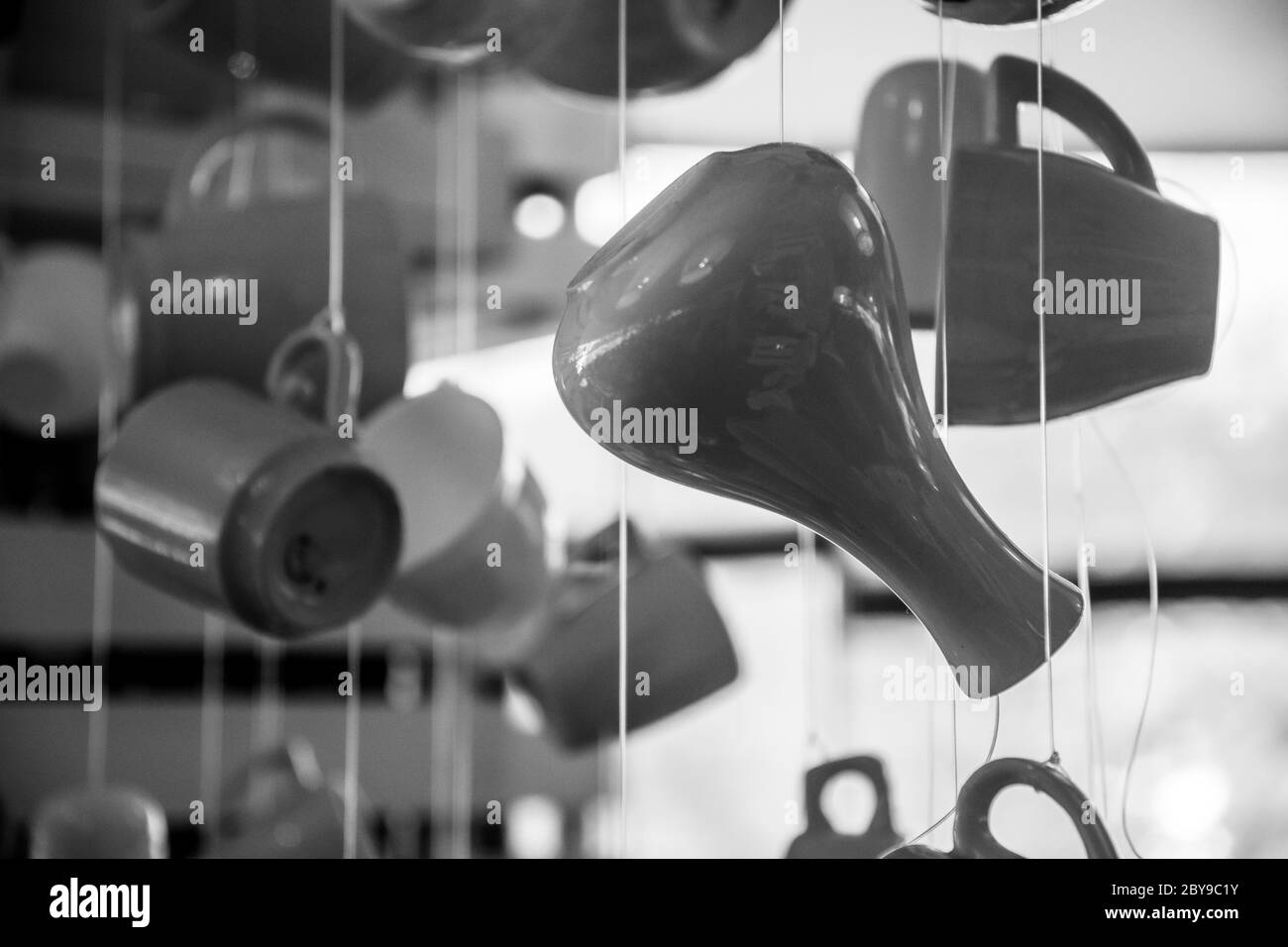 Foto monocromatica di silhouette di utensili da cucina. Vaso in ceramica, tazze da caffè e tazze da tè appesi a corde alla luce del sole. Caffè del mattino e. Foto Stock