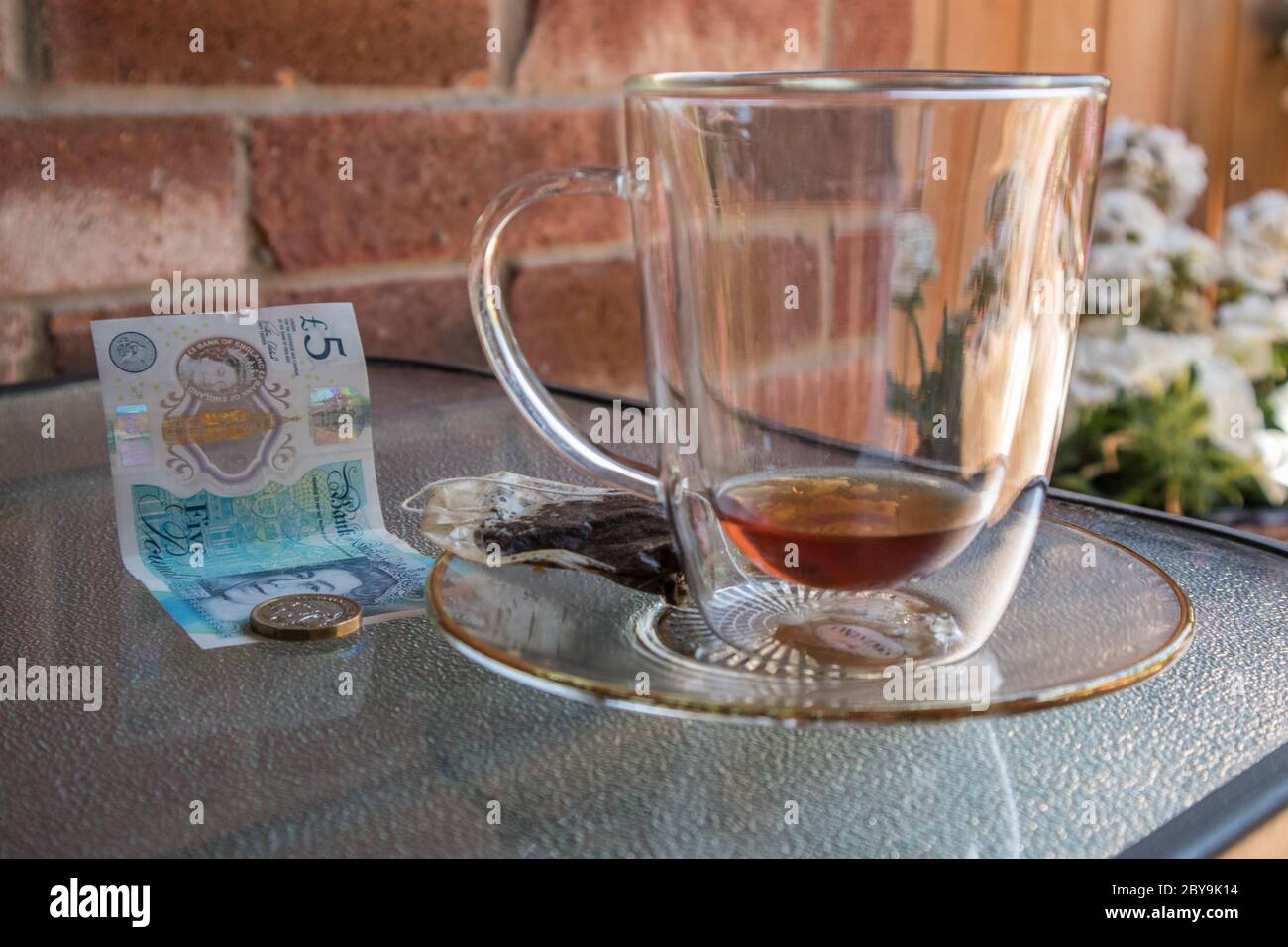 Una caffetteria o una terrazza durante l'estate. Sulla tavola una tazza di tè trasparente vuota e alcune libbre, probabilmente la punta. Foto Stock