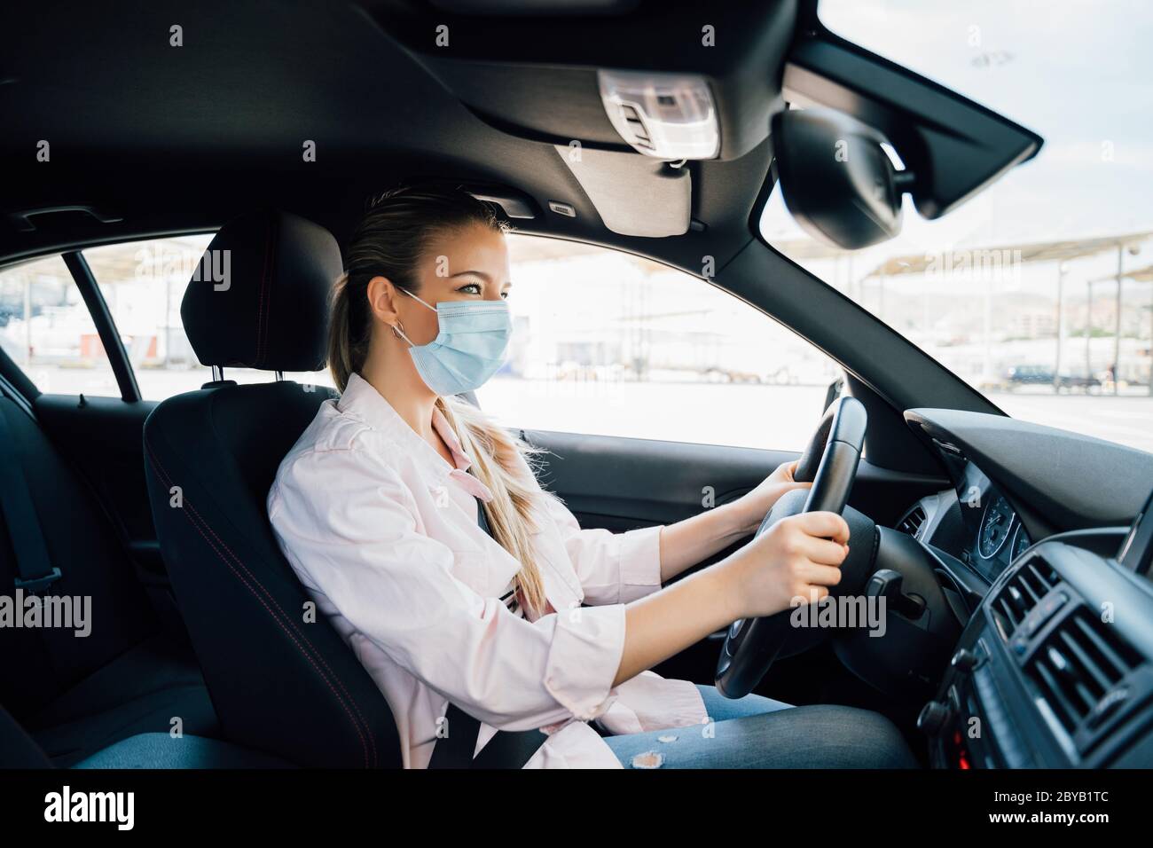 Donna con maschera facciale che guida la sua auto durante la pandemia di coronavirus Foto Stock