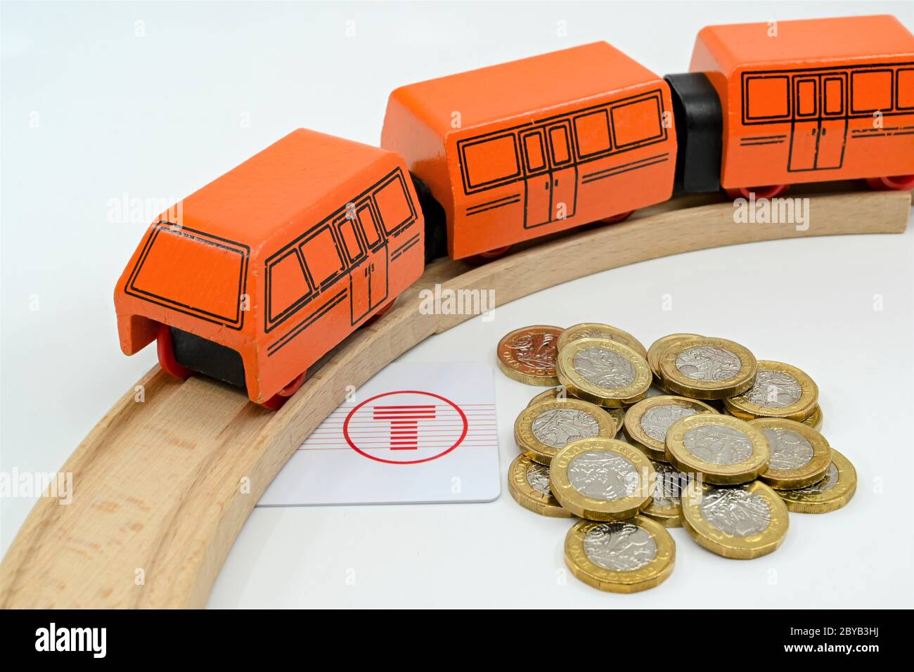 CARDIFF, GALLES - GENNAIO 2020: Pila di monete da una libbra accanto a un treno di legno e una carta di viaggio emessa da Transport for Wales. Foto Stock