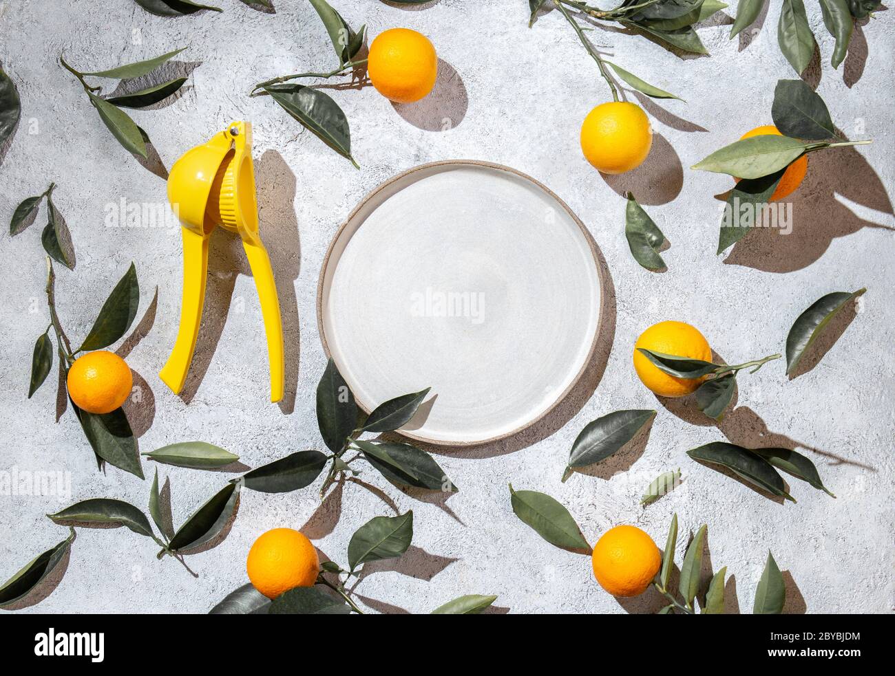 Arance intere con foglie di arance e centrifuga su sfondo bianco intorno al piatto vuoto. Vista dall'alto, piatto, estate e sano. Foto Stock