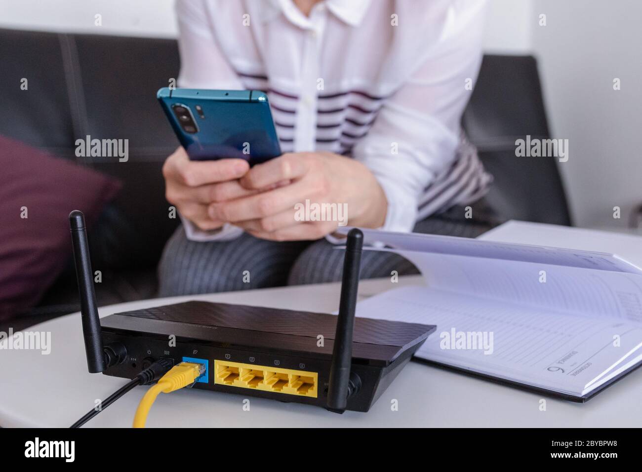 primo piano di un router wifi e una donna che utilizza uno smartphone nel salotto di casa ofiice Foto Stock
