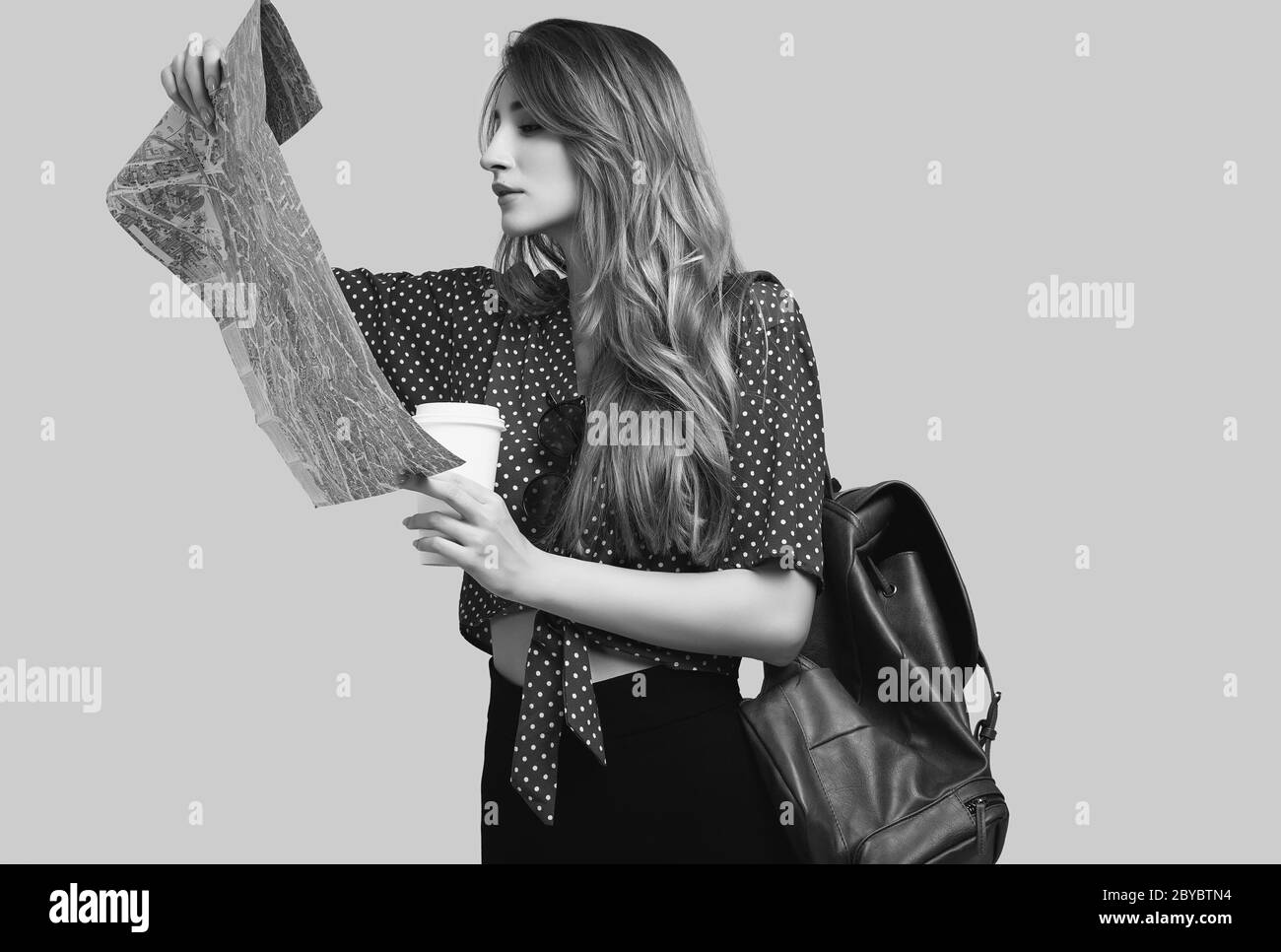 Concetto di viaggio. Sognare il viaggio. Studio ritratto di bella giovane donna hipster con zaino tenendo mappa. Isolato su sfondo grigio Foto Stock