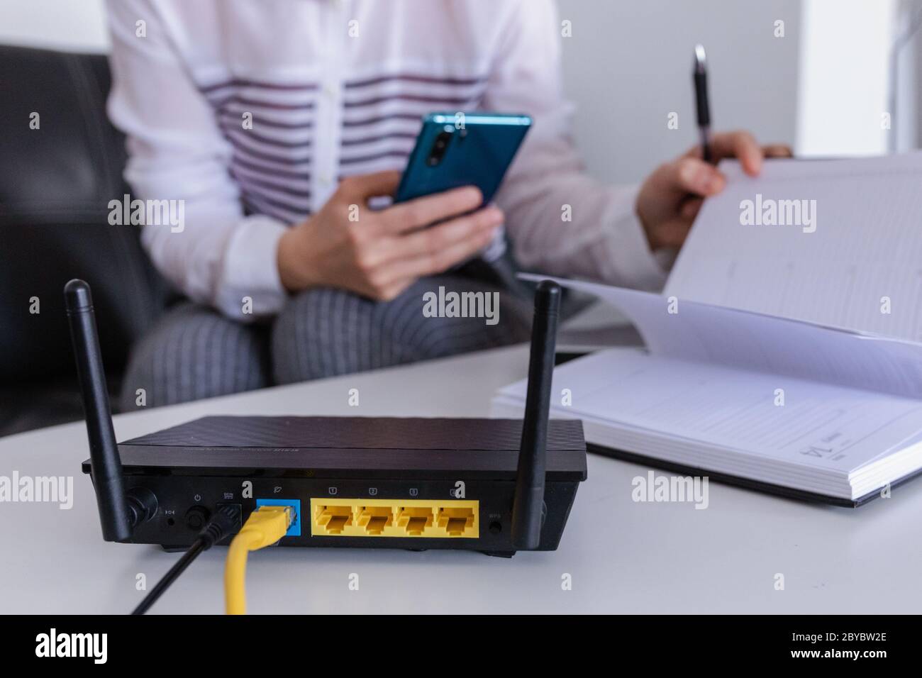 Router wireless e donna che usa un telefono in ufficio. Router wireless a banda larga casa computer portatile telefono wifi concetto Foto Stock