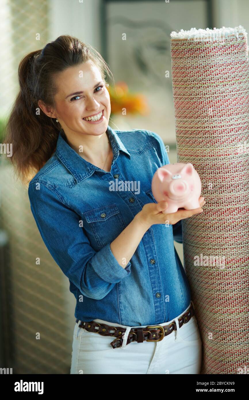 donna moderna sorridente in camicia jeans e pantaloni bianchi con tappeto  bianco che mostra la banca piggy a casa moderna in giornata di sole Foto  stock - Alamy