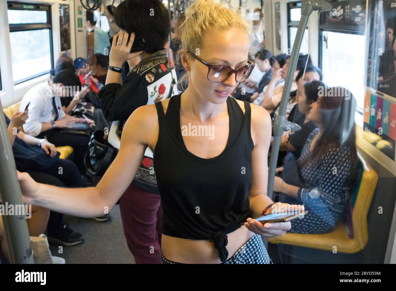 Viaggiatore caucasico femminile utilizzando il telefono cellulare sulla metropolitana di trasporto pubblico a Kuala Lumpur, capitale della Malesia Foto Stock