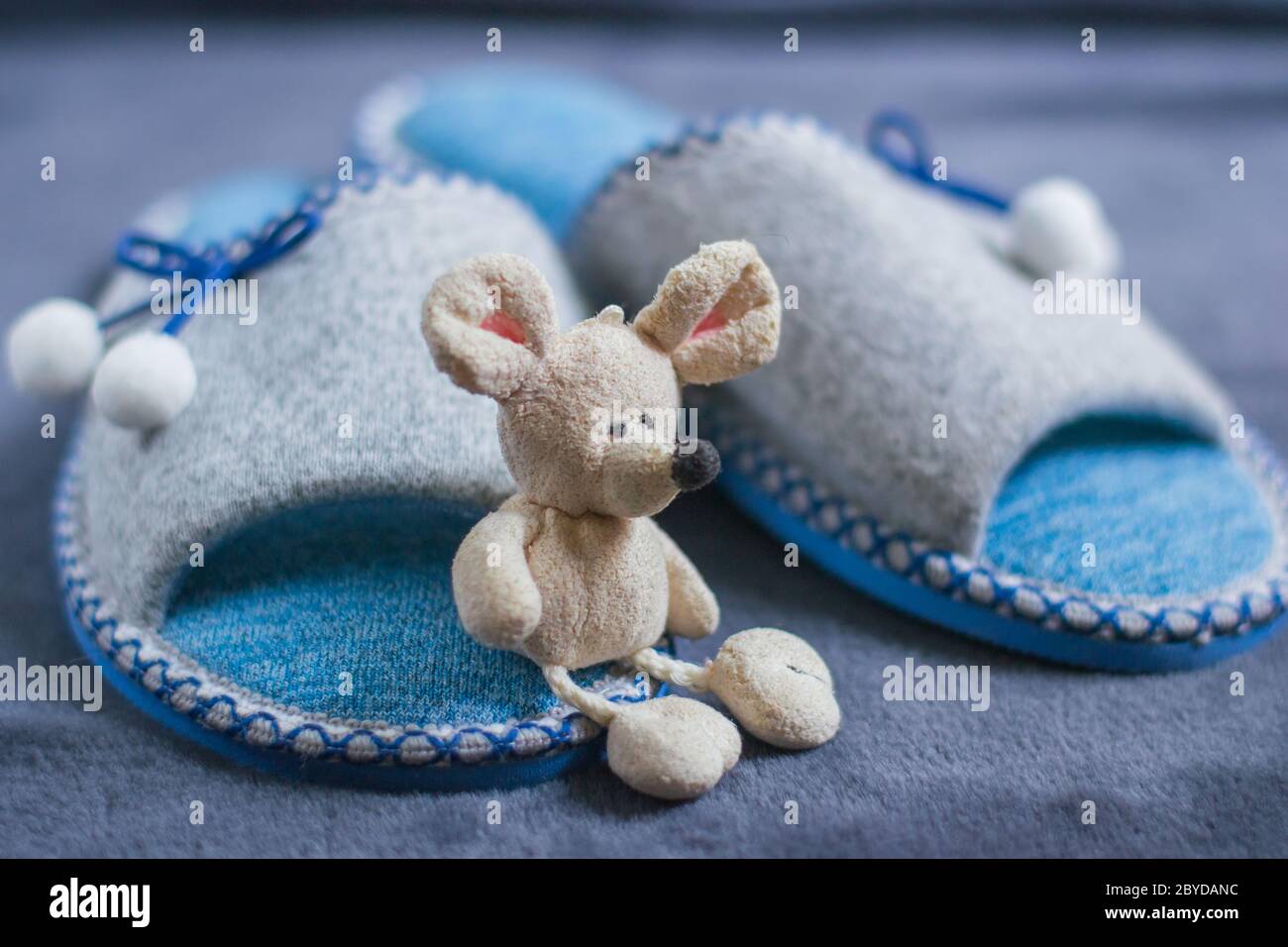 Un mouse giocattolo si trova sulle pantofole con i pompon in piedi su un tappeto soffice. Abbigliamento e scarpe per donne o bambini. Il concetto di calore domestico. Foto Stock
