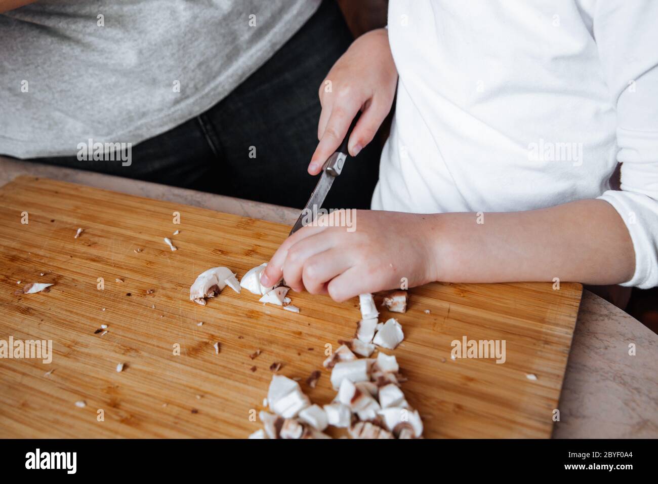 Funghi champignon freschi su tavola di legno. Una ragazza e la madre tagliarono i funghi con un coltello. Tempo trascorso insieme. Concetto di famiglia Foto Stock