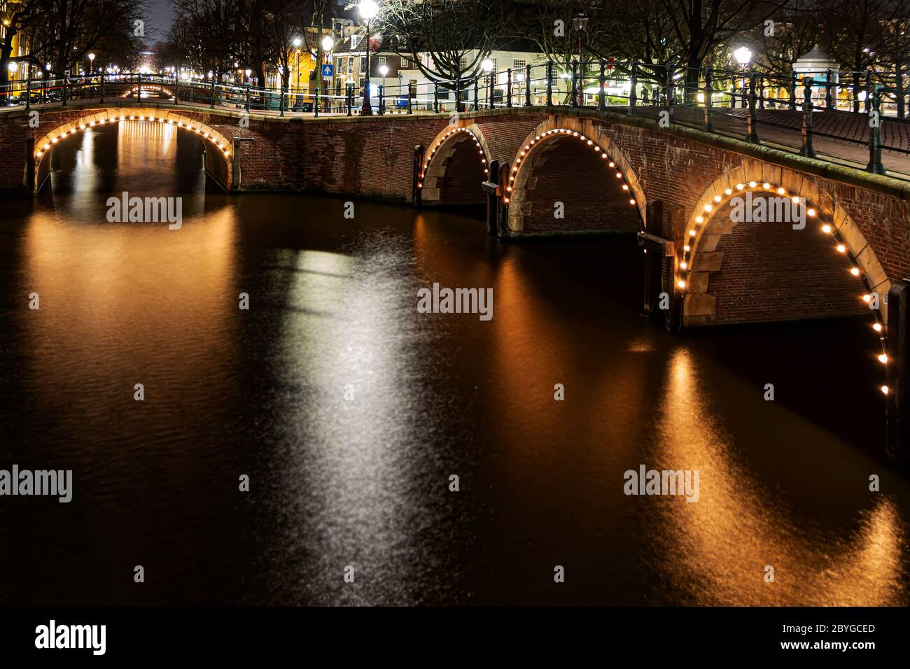 Il ponte illuminato sui canali di Amsterdam si riflette sulla calma acqua del canale di Amsterdam di notte Foto Stock
