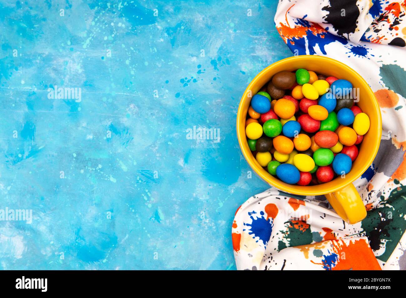 Draghi multicolore in una tazza e un panno colorato su sfondo blu. Vista dall'alto, spazio di copia. Stile di vita luminoso e vivace. Foto Stock