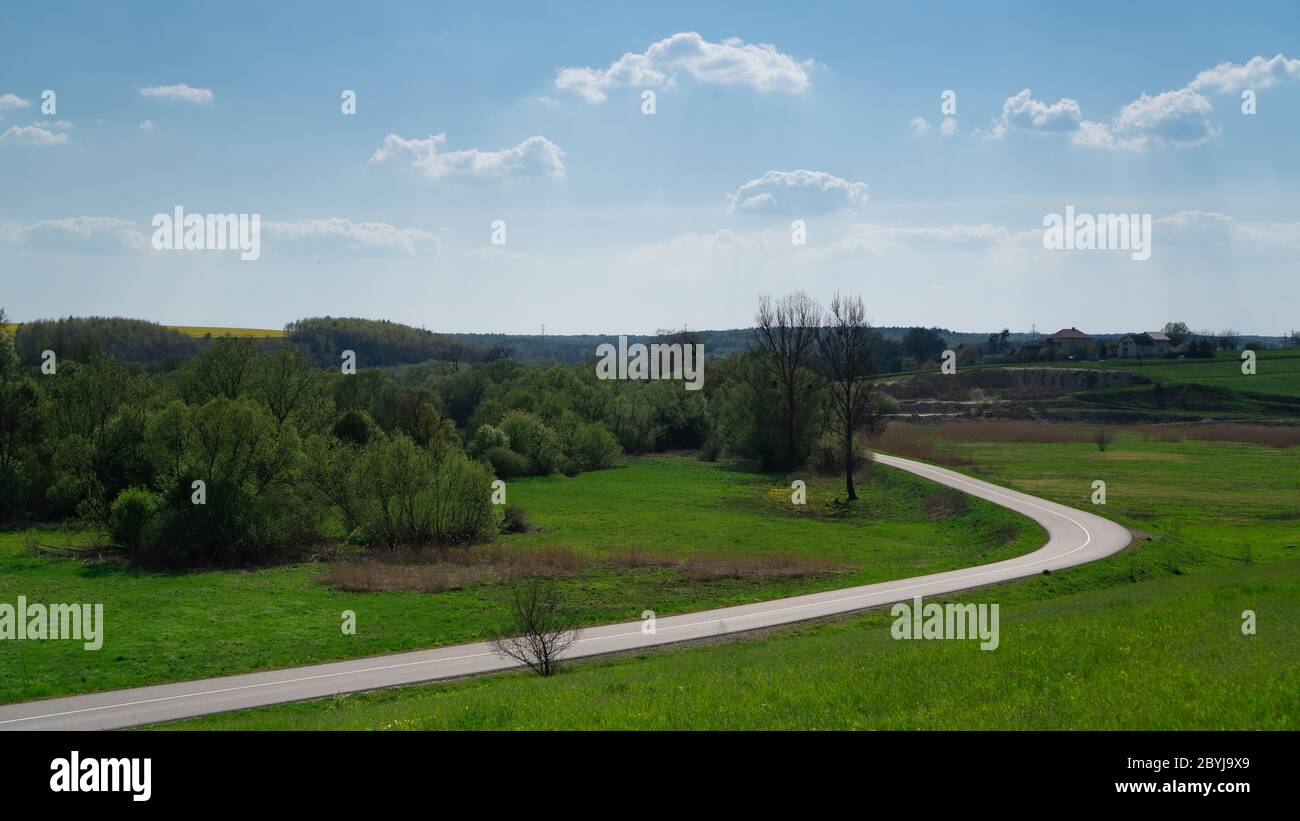 Strada di campagna in Ucraina. Campi verdi e cielo blu. Tortuosa strada di campagna tra prati e alberi. Giorno chiaro Foto Stock