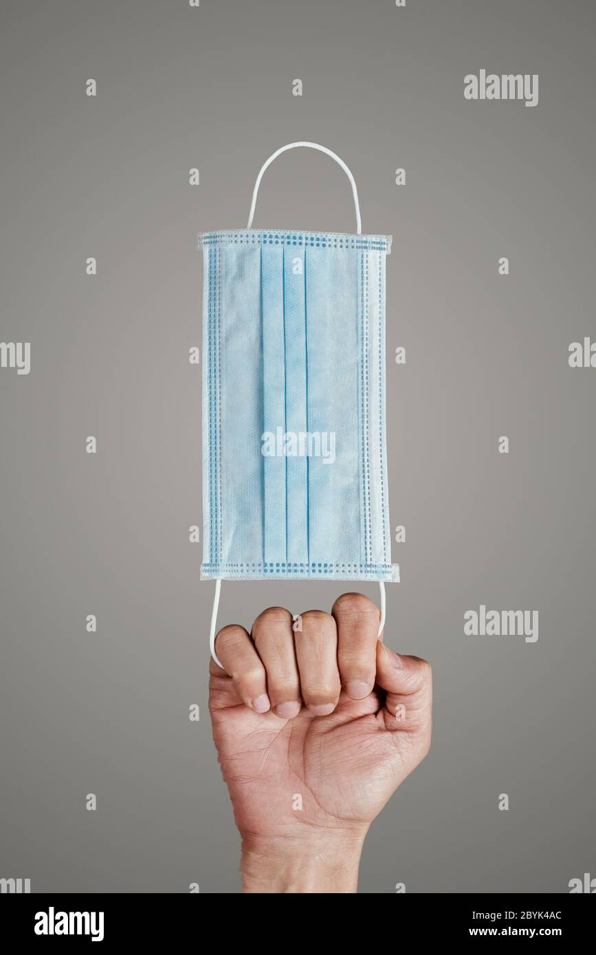 primo piano di un giovane caucasico con una maschera chirurgica in mano, su sfondo grigio Foto Stock