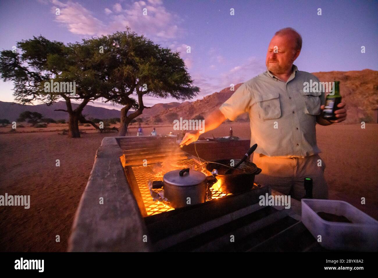 Un membro della festa di viaggio che cucinava del cibo per tutti, Helmeringhausen, Namibia Foto Stock