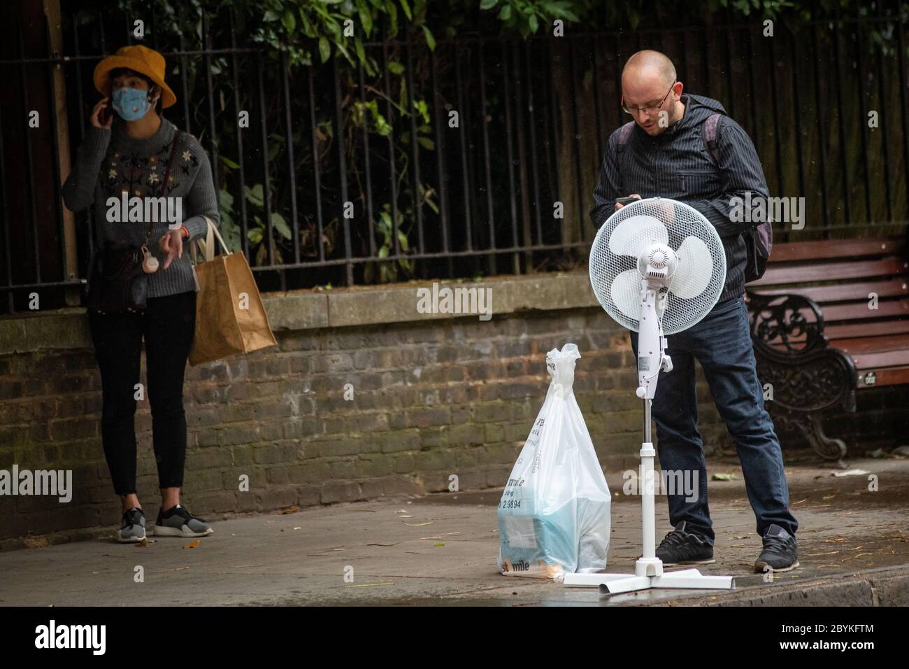 Un uomo attende un autobus con un ventilatore vicino a Kensington Gardens, mentre il Regno Unito dovrebbe essere colpito con forti docce, forti galere e temperature più fredde nel weekend, con i britannici che sono stati avvertiti di non spostare le riunioni all'interno. Foto Stock