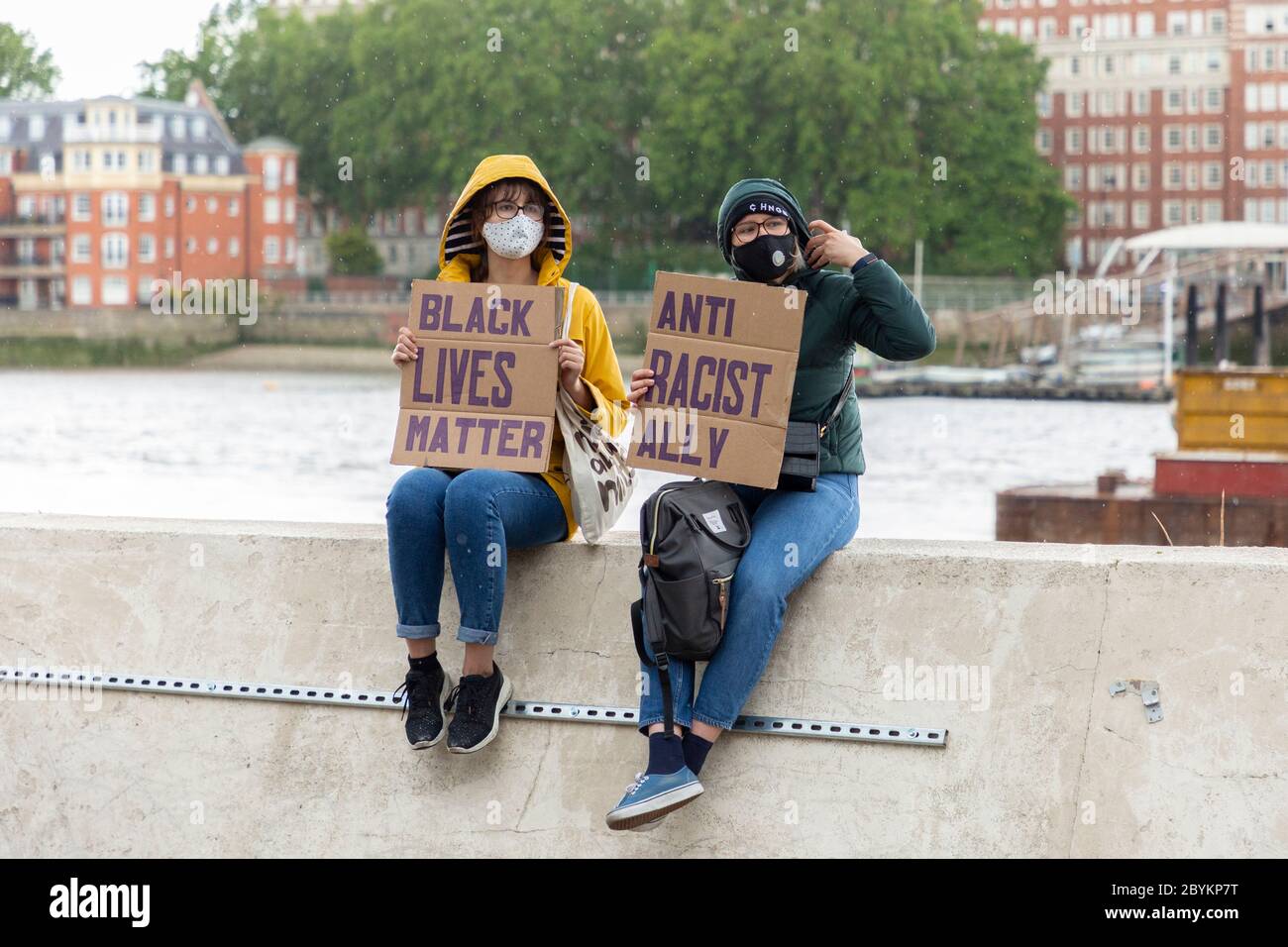 Due manifestanti seduti accanto al Tamigi che reggono i cartelli, Black Lives Matters protesta, Nine Elms, Londra, 7 giugno 2020 Foto Stock