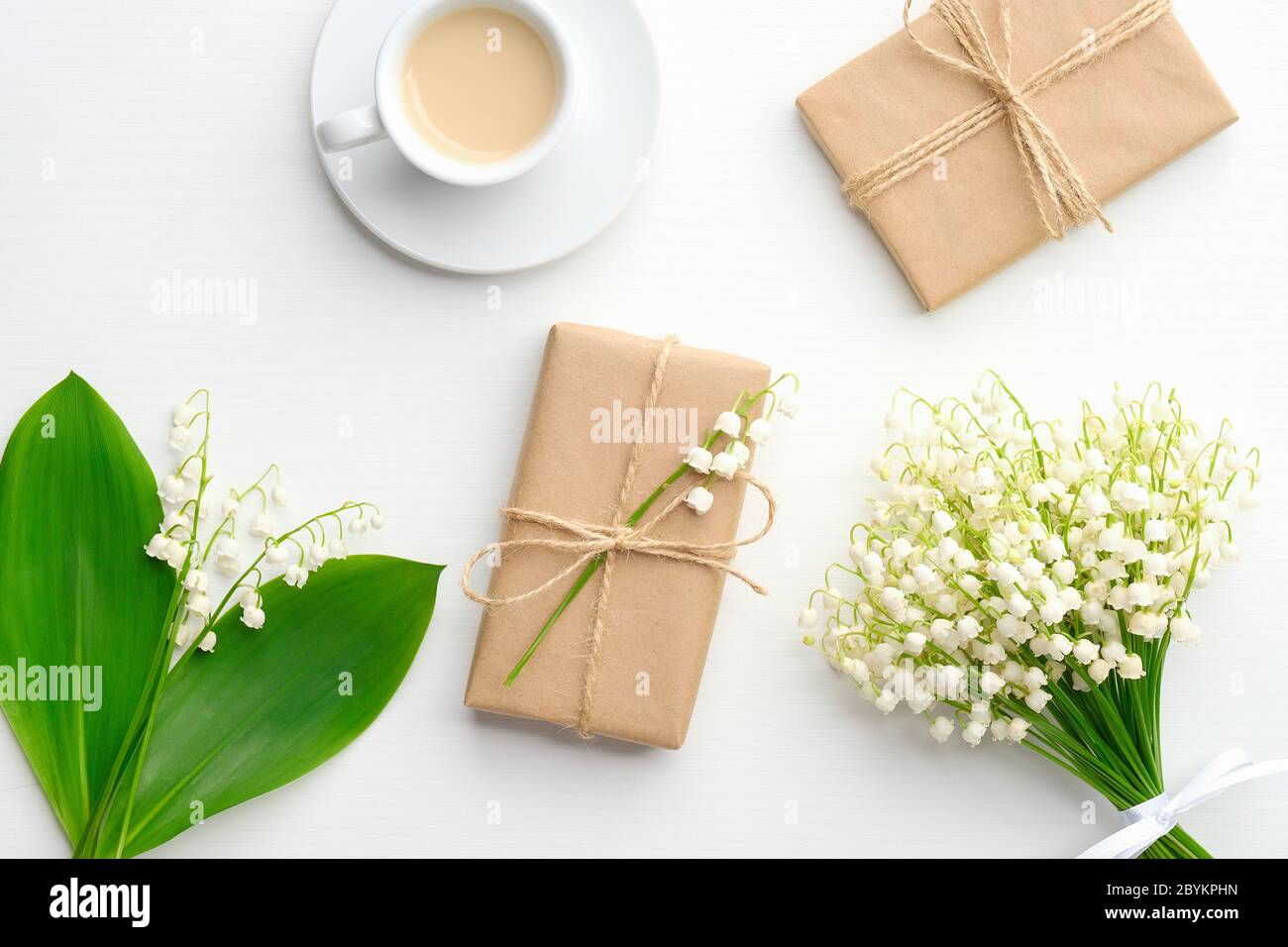 Scatole regalo carta kraft avvolta, caffè della mattina e giglio di fiori della valle su tavola bianca dall'alto. Concep di festa di nozze o anniversario Foto Stock