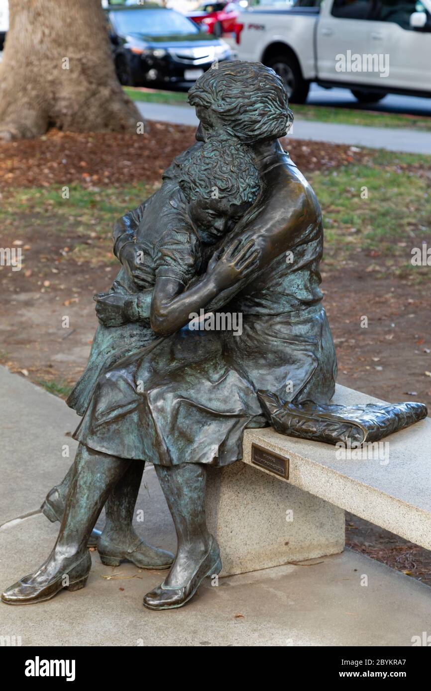 Donna che conforta la statua di bronzo del bambino al memoriale degli ufficiali di Pace, 10th Street, Sacramento, California, Stati Uniti d'America Foto Stock