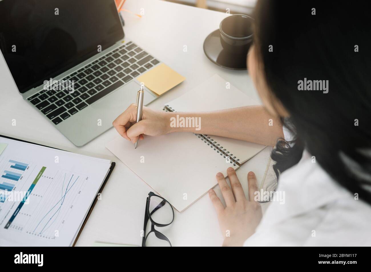 donna attraente che scrive in blocco note mentre guarda il webinar su un notebook Foto Stock
