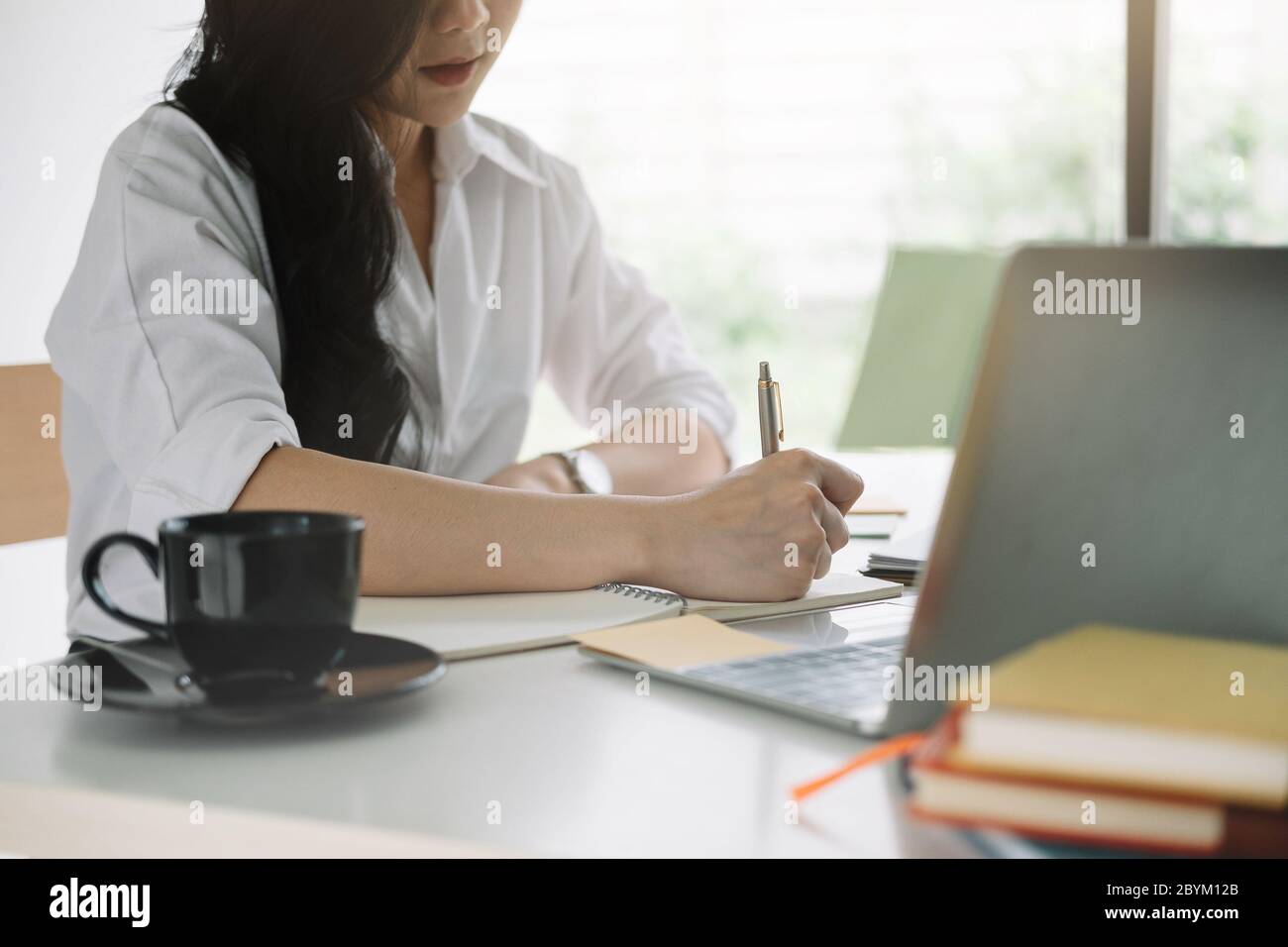 donna attraente che scrive in blocco note mentre guarda il webinar su un notebook Foto Stock