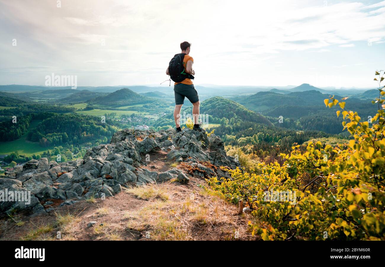 Uomo escursioni in cima a una montagna rocciosa. Ripida scogliera, parte rocciosa del percorso con vista in lontananza. Paesaggio panoramico delle montagne di Lunation, ceco Foto Stock