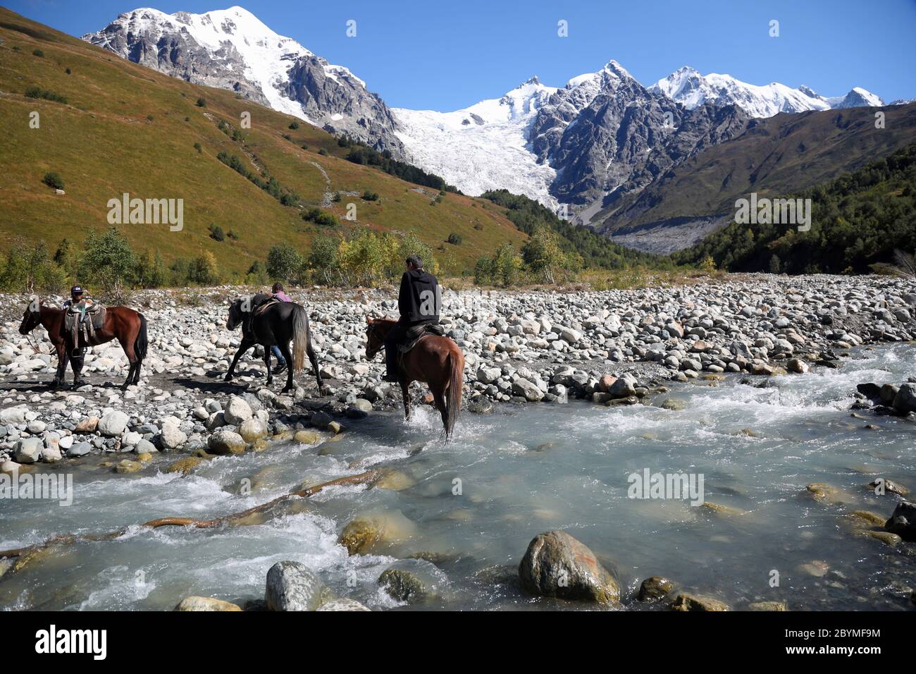 12.09.2019, Adishi, Swaanetia, Georgia - uomini che attraversano un fiume glaciale sui loro cavalli a Tetnuldi. 00S190912D236CAROEX.JPG [VERSIONE DEL MODELLO: NO, PROPERTT Foto Stock