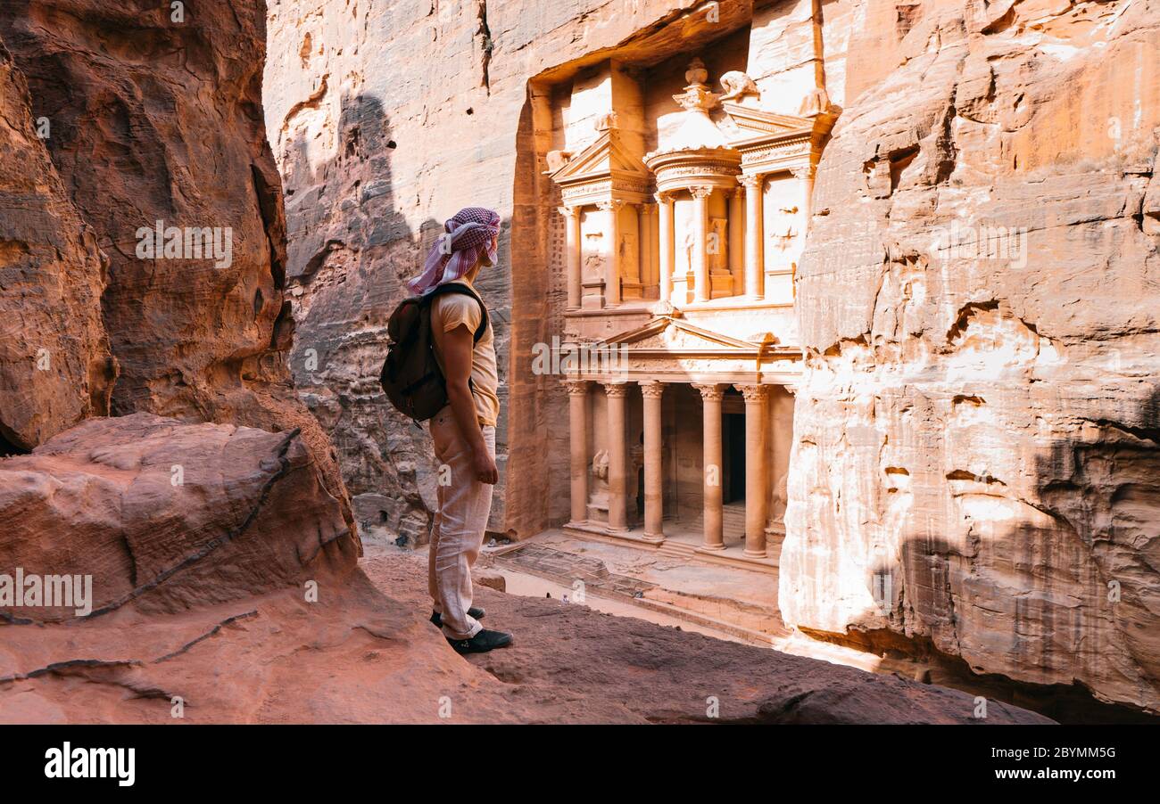 L'uomo avventuroso si trova sulla cima della roccia e gode di una splendida vista durante un tramonto vibrante. In cima a Petra, Giordania. UNESCO Foto Stock