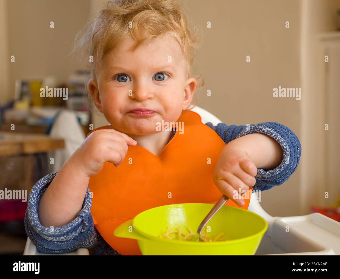 Bambino di un anno con espressione divertente mangiare con posate a casa Foto Stock