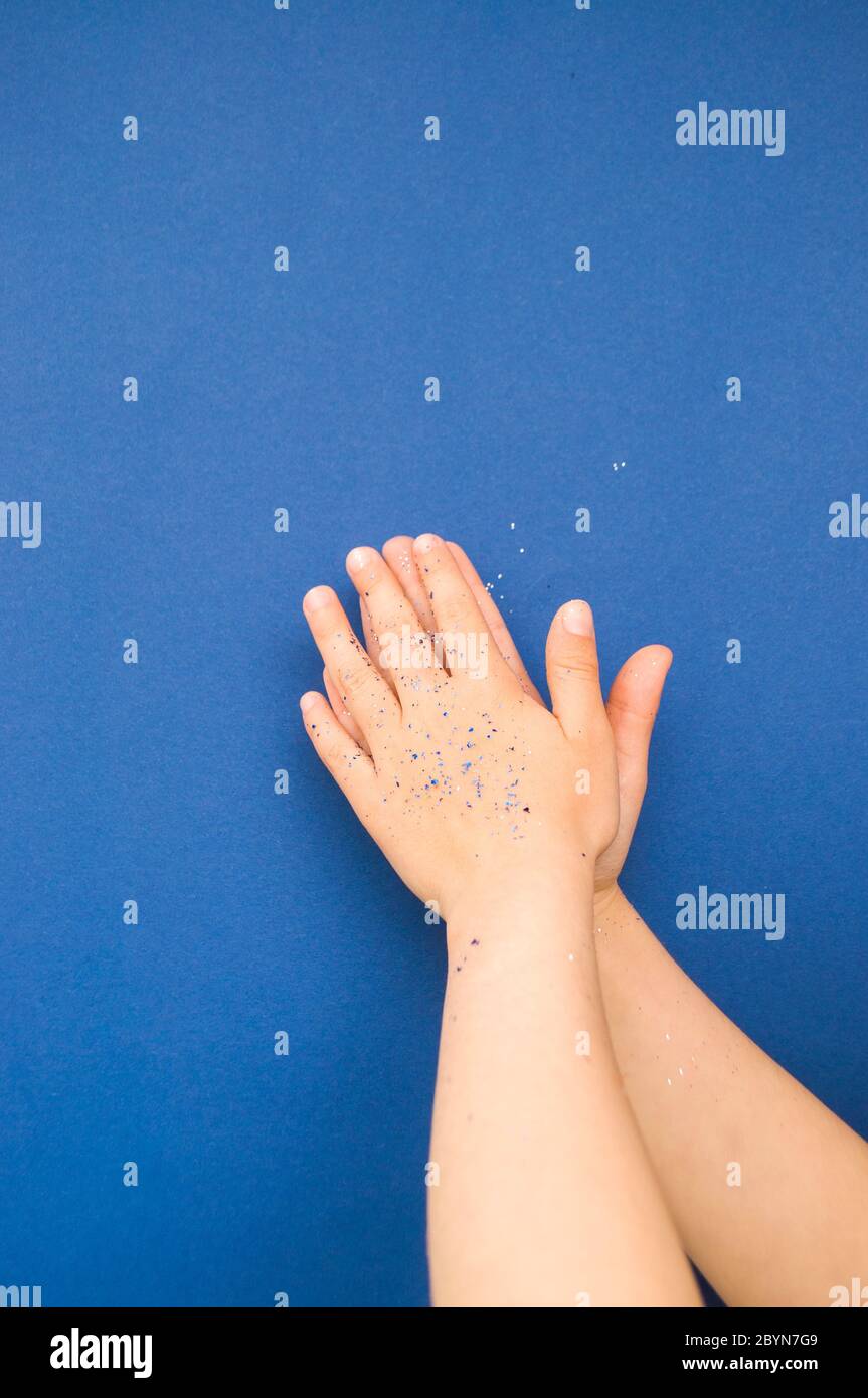 Mani per bambini con glitter e confetti di colore blu e argento su sfondo blu classico. Foto Stock