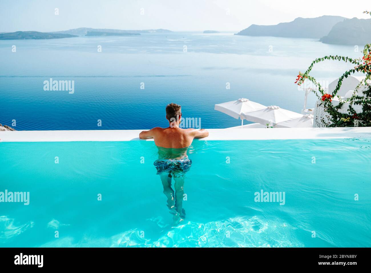 Santorini Grecia Oia, giovani uomini in nuotata breve relax in piscina con vista sulla caldera dell'isola di Santorini grecia, piscina infinity Grecia Foto Stock