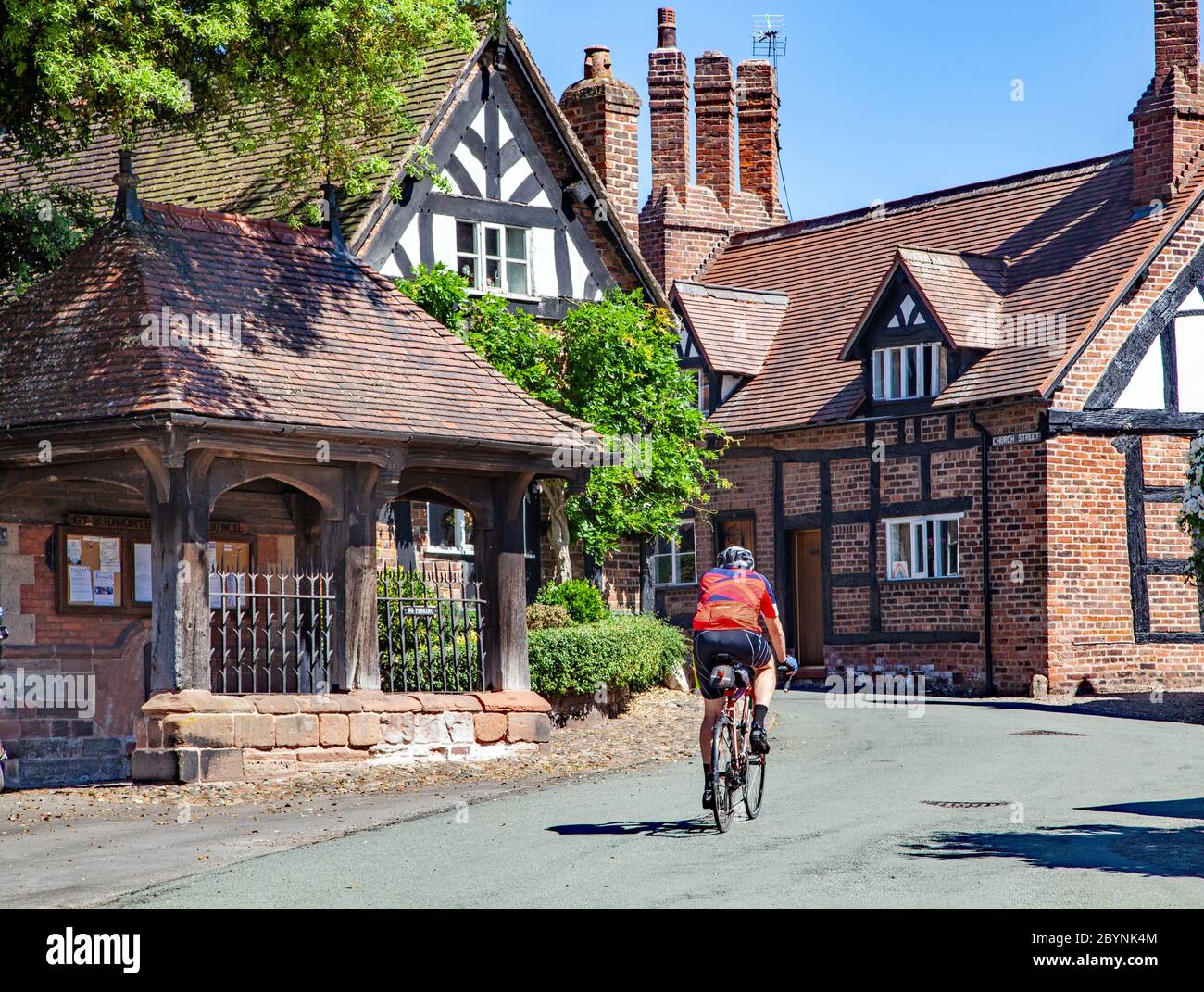 Uomo in bicicletta attraverso il pittoresco villaggio di Cheshire, un antico paese rurale, idilliaco e quintessenza, di Great Budworth Inghilterra UK Foto Stock