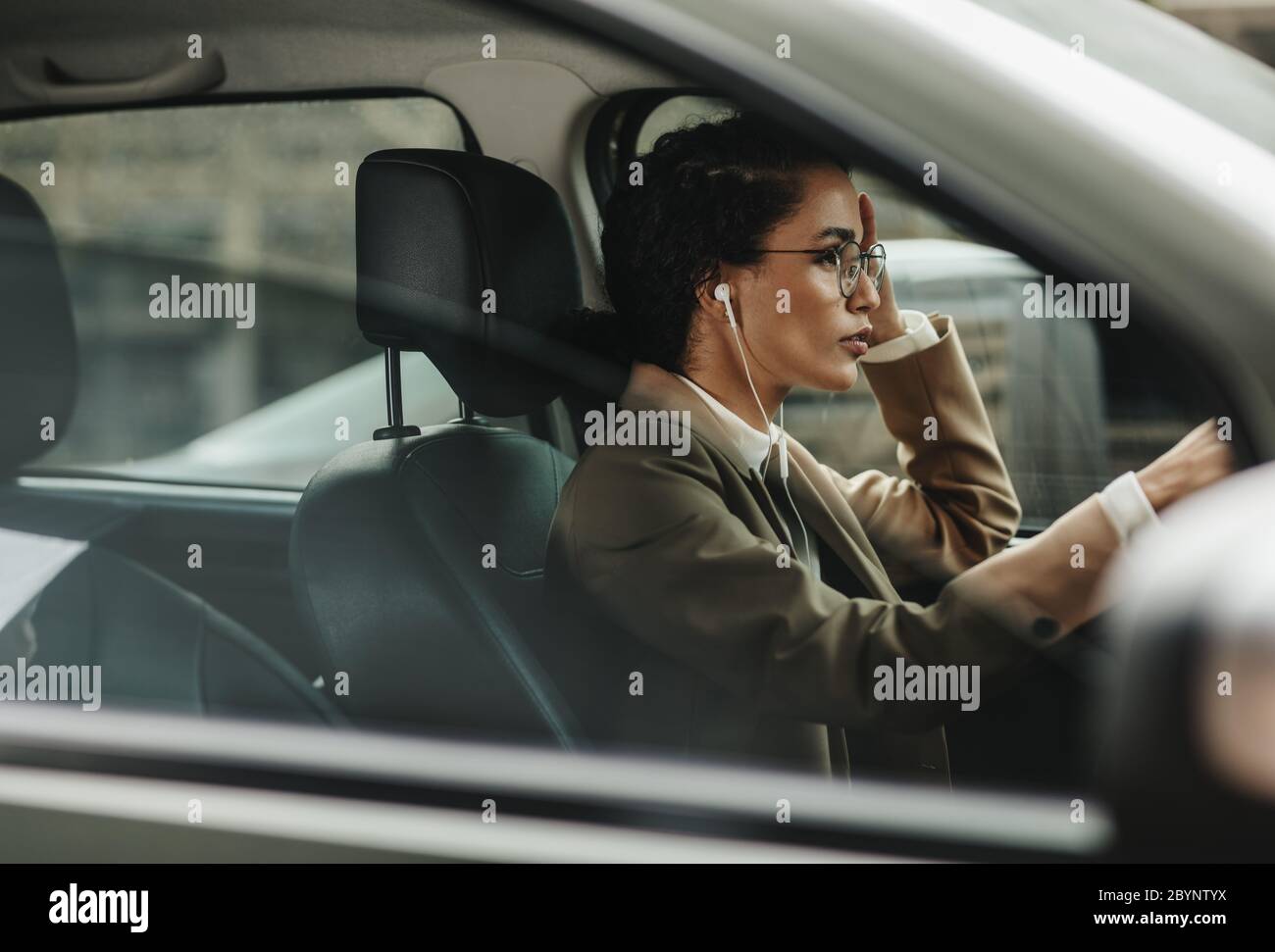 Donna d'affari con auricolari che guidano la sua automobile all'ufficio. Donna in abbigliamento da formalwear che guida al lavoro. Foto Stock