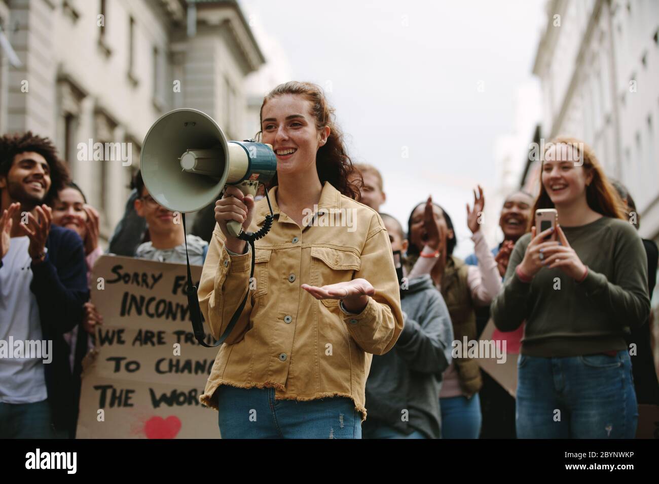Donna con un megafono in un rally all'aperto su strada. Donna in piedi all'aperto con un gruppo di dimostranti che si aggrappano e festeggiano. Foto Stock