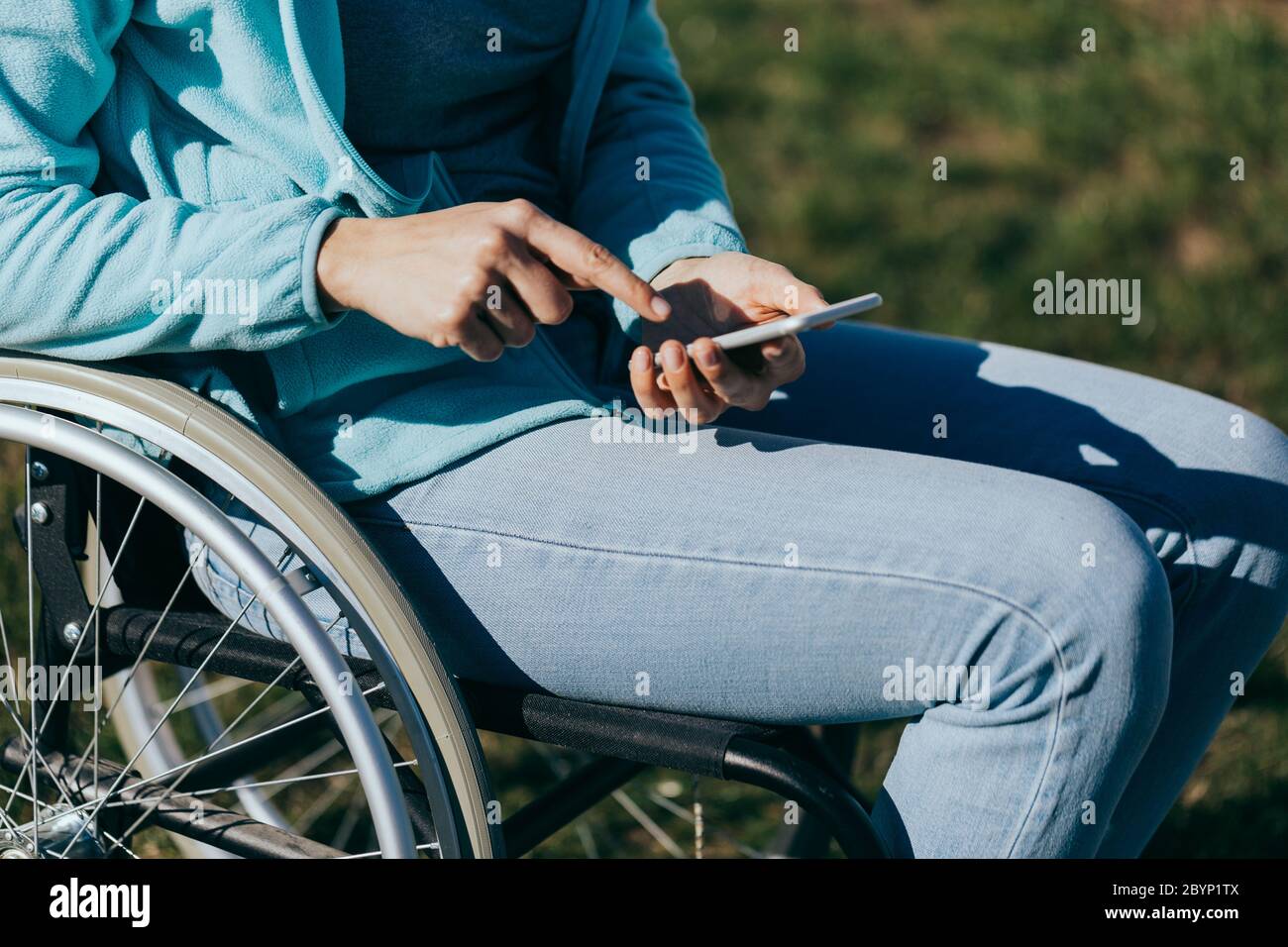 Una donna in sedia a rotelle con un telefono in mano cammina per strada, la sua mano è vicina, un irriconoscibile Foto Stock