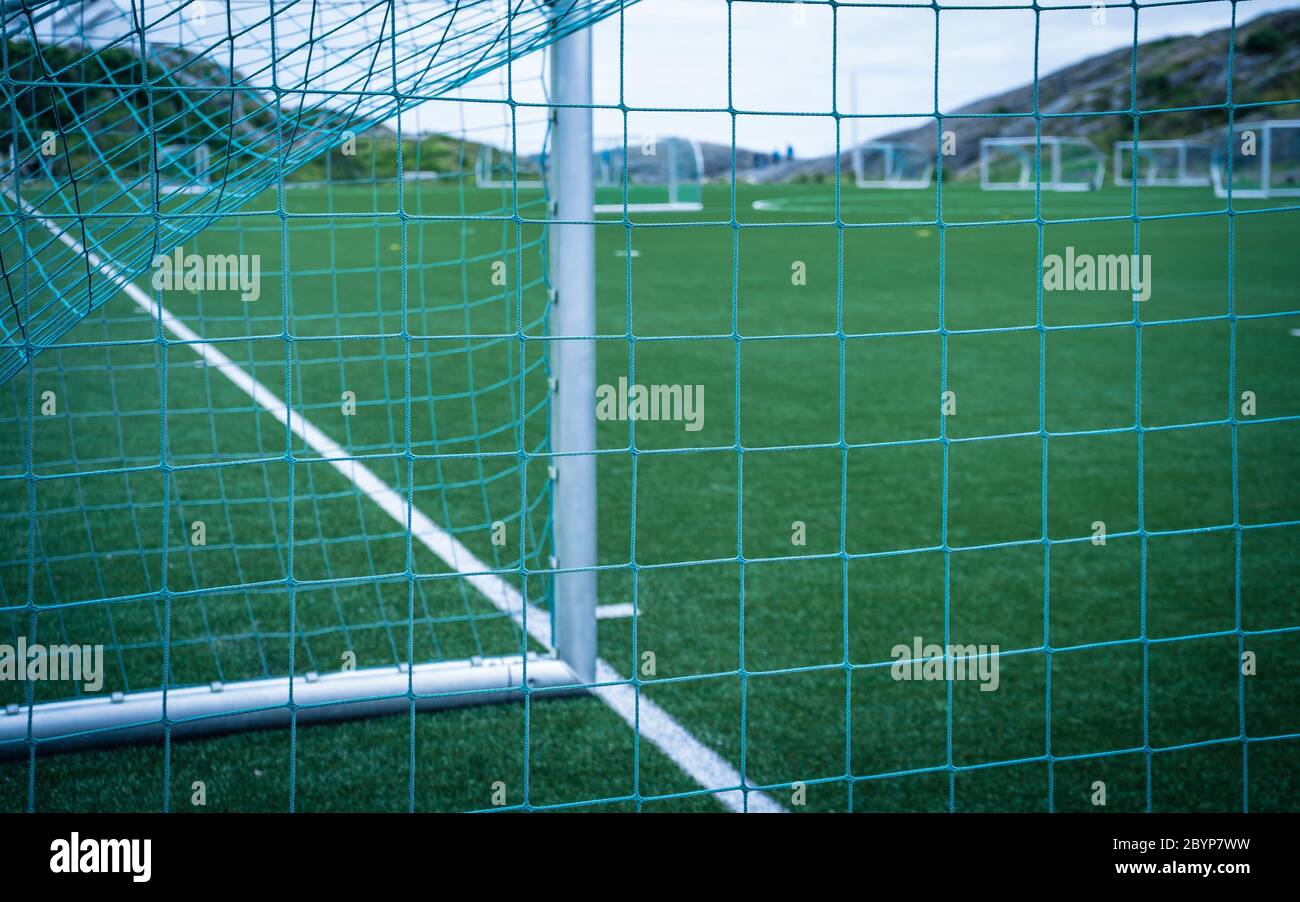 Linee intorno al campo da calcio, lato angolo, in prato sintetico. Vista dietro la rete sul campo di calcio sulle isole Lofoten circondato da rocce Foto Stock