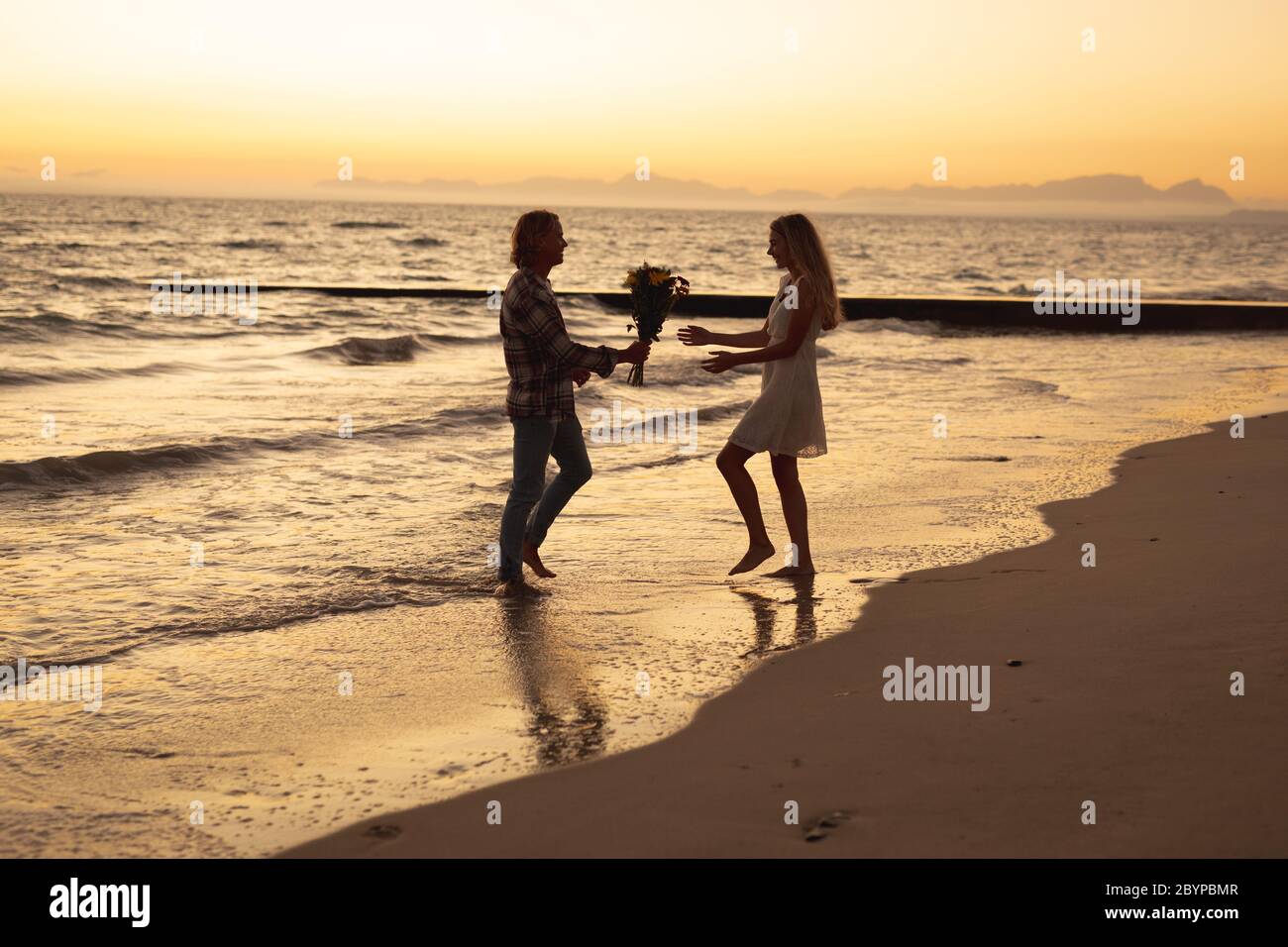 Coppia caucasica che si gode del tempo su una spiaggia durante il tramonto Foto Stock