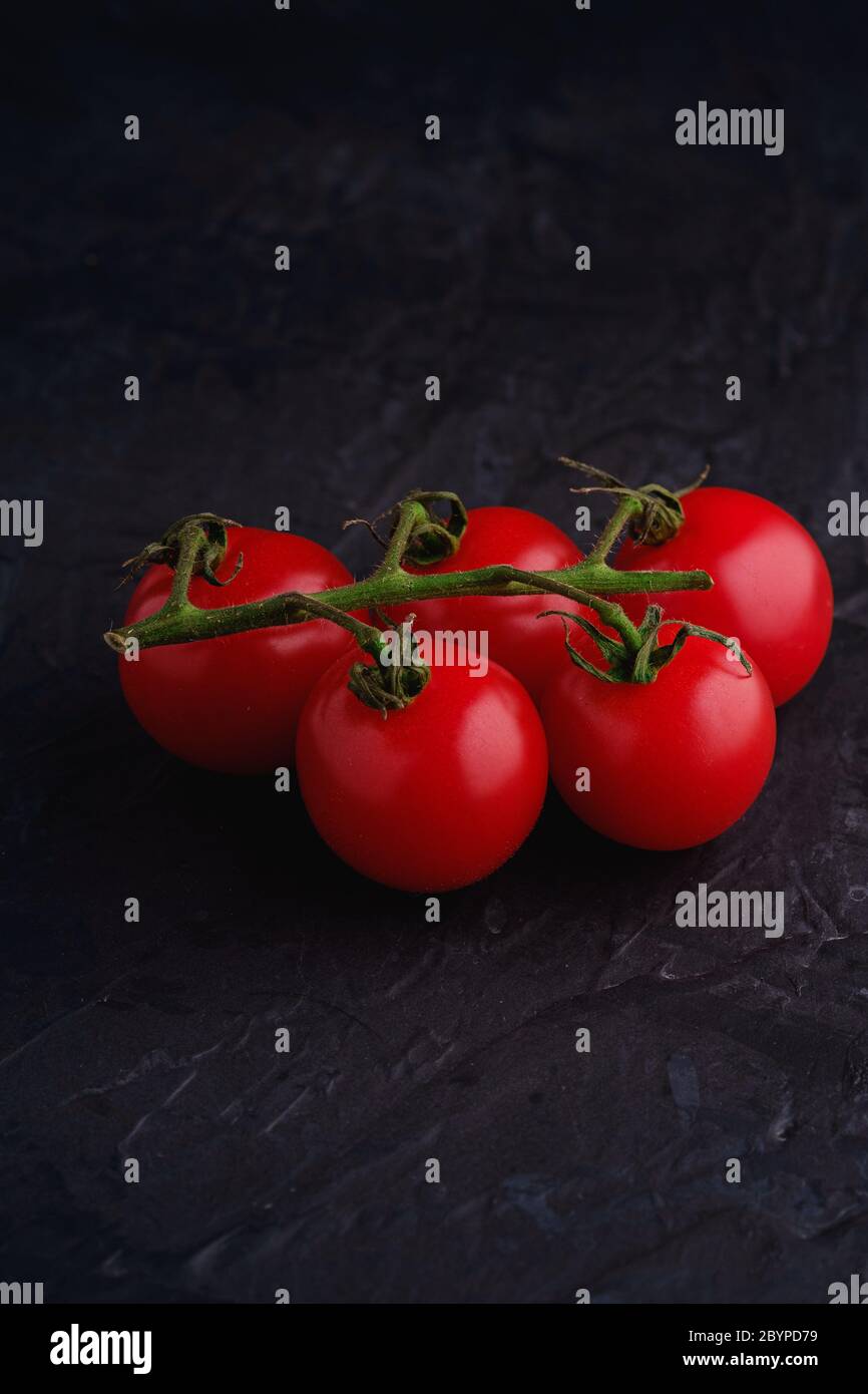 Rametto di pomodoro di ciliegio, verdure biologiche fresche mature su sfondo nero scuro con texture, vista macro-angolo Foto Stock