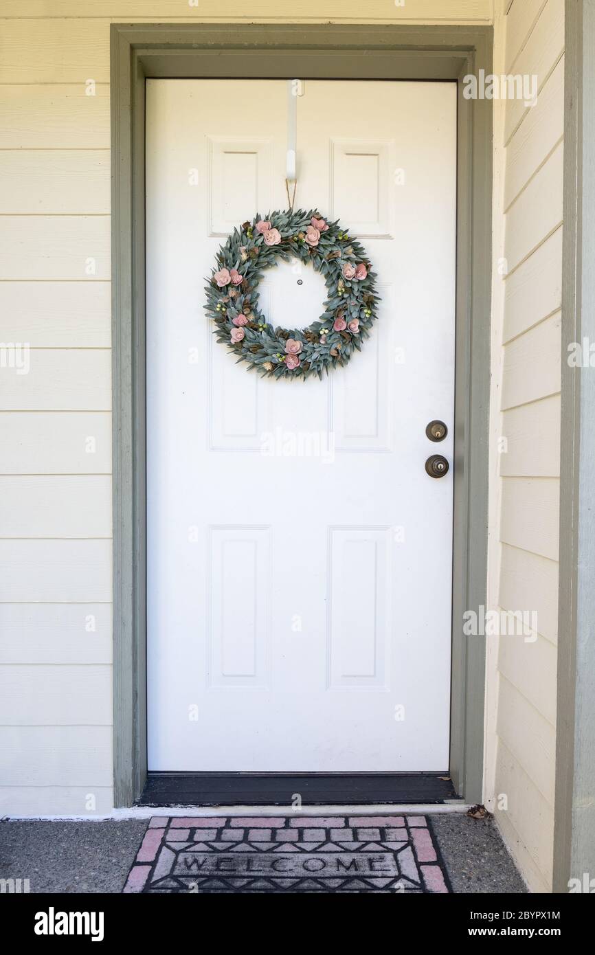 Porta anteriore della casa con la corona decorativa e il tappetino di benvenuto Foto Stock