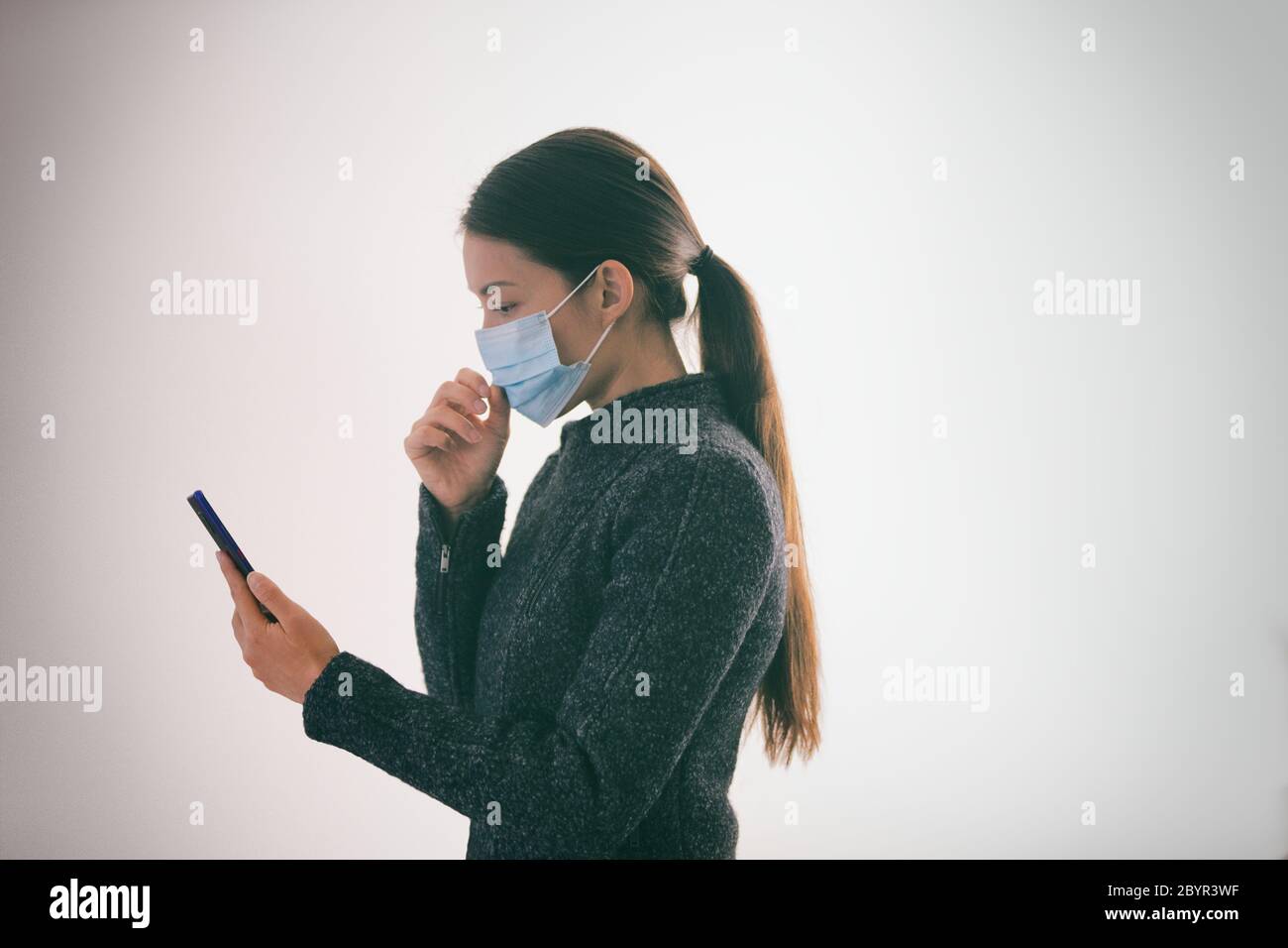 COVID-19 applicazione di tracciamento dei contatti sul telefono cellulare donna che cammina all'esterno mentre si indossa una maschera medica chirurgica a contatto con il viso testando smartphone Foto Stock